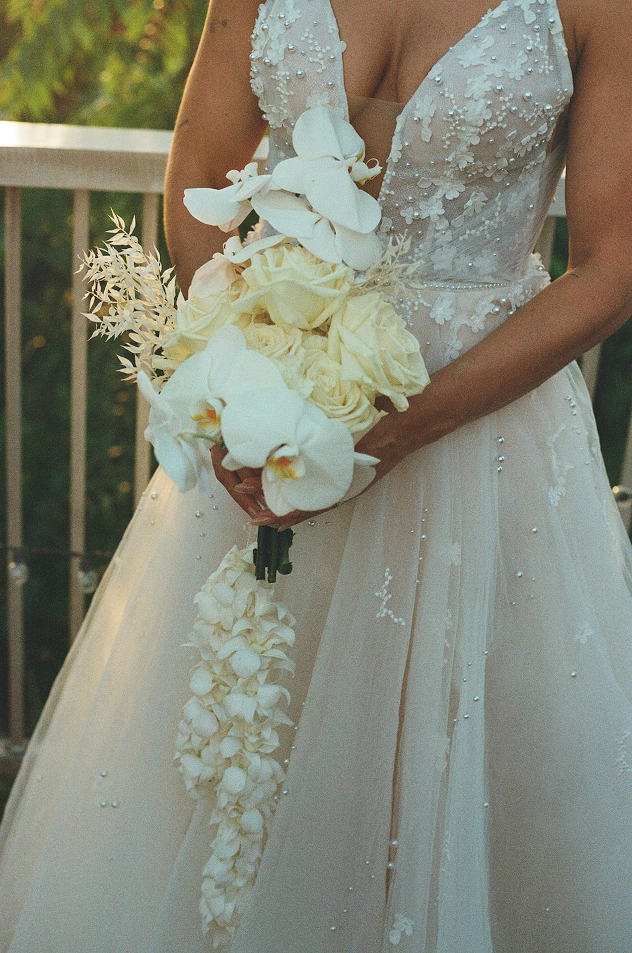 Close-up of the bride holding a cascading bouquet of white orchids and roses against her detailed gown.