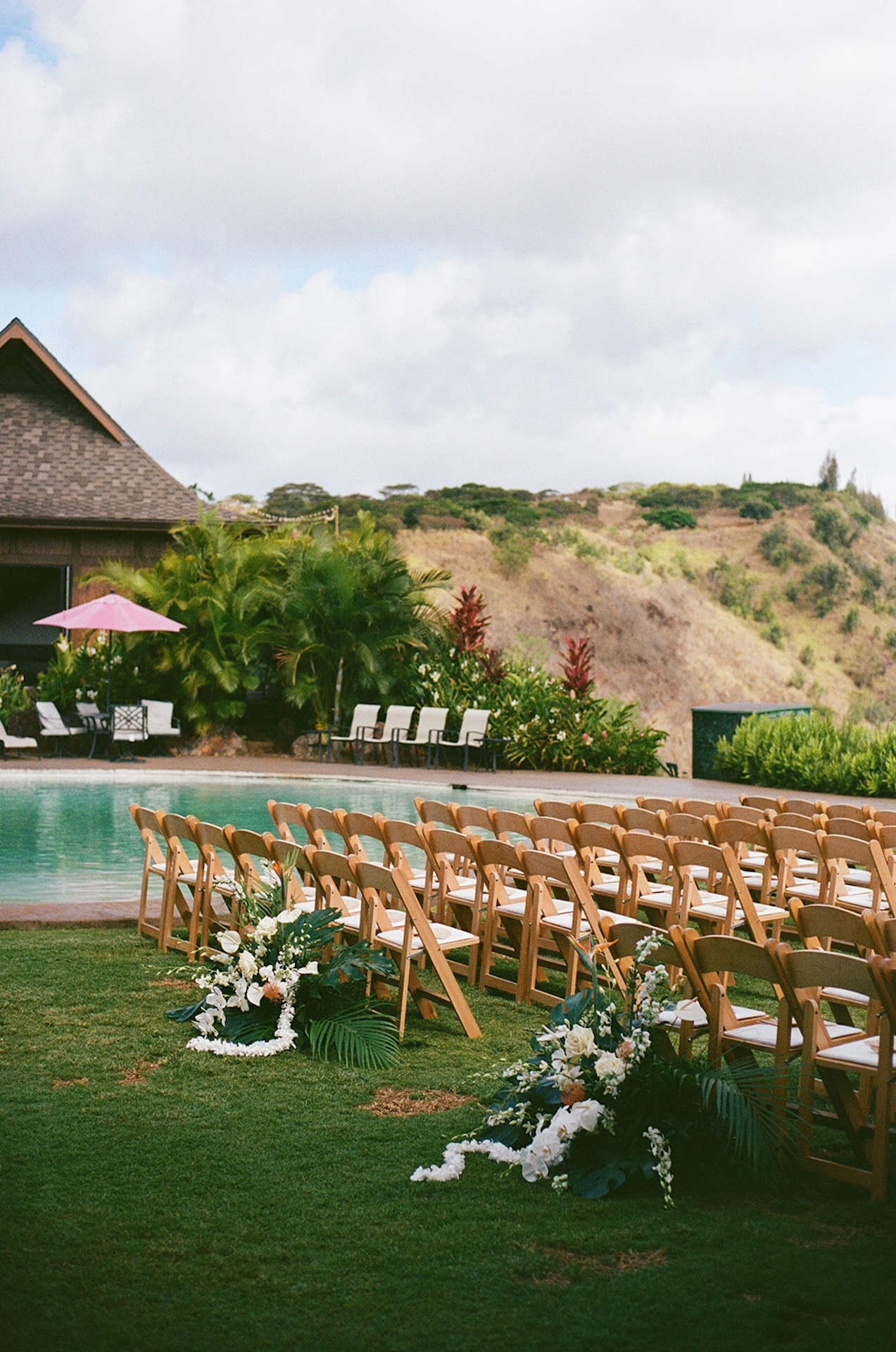 Wedding ceremony setup by the pool with tropical florals and rows of chairs facing a mountain view, a breathtaking scene at Wedding Venues in Hawaii.