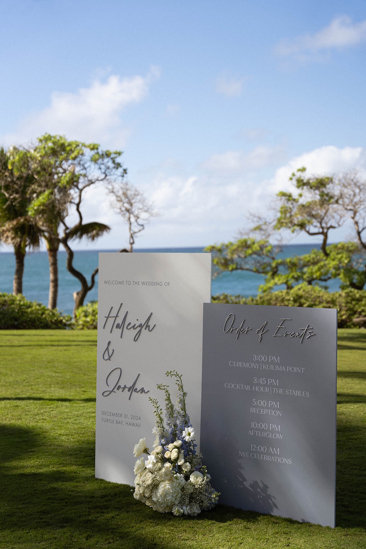 Wedding welcome signage and order of events board on the lawn, featuring the couple’s names and a detailed wedding weekend itinerary, accented with white and blue florals.