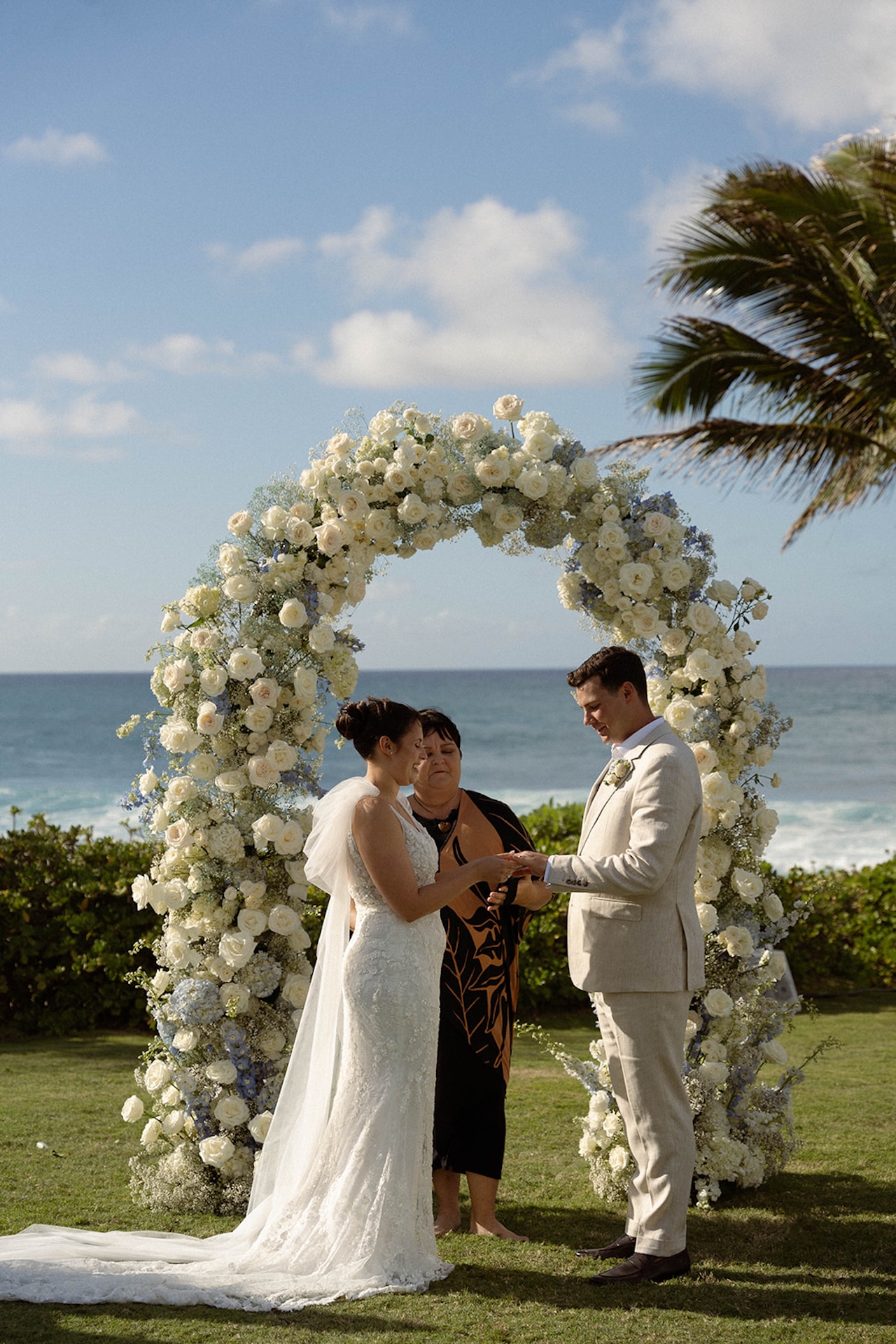 A close-up of the couple exchanging rings under the flower arch, capturing the intimacy of their Hawaii beachside ceremony.