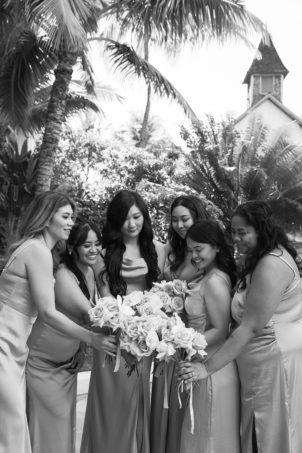 Black-and-white photo of bridesmaids in satin dresses gathering around with matching white bouquets, a sweet memory from their Destination wedding checklist.