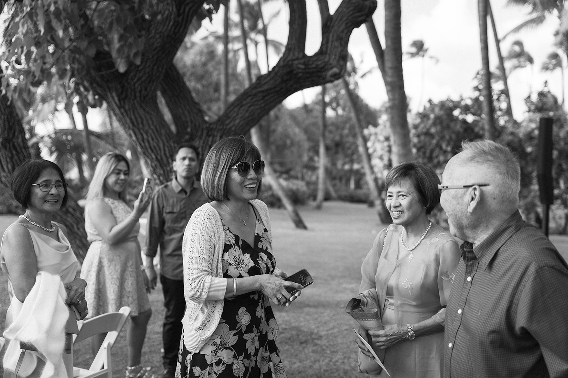 Guests chatting and laughing together under the trees before the ceremony begins, enjoying the relaxed island atmosphere.
