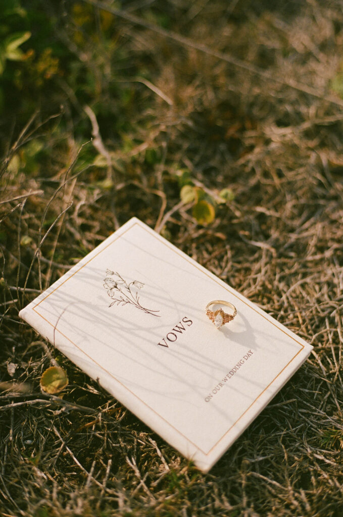 The bride and grooms vows book with a wedding ring resting on it in a field of grass.