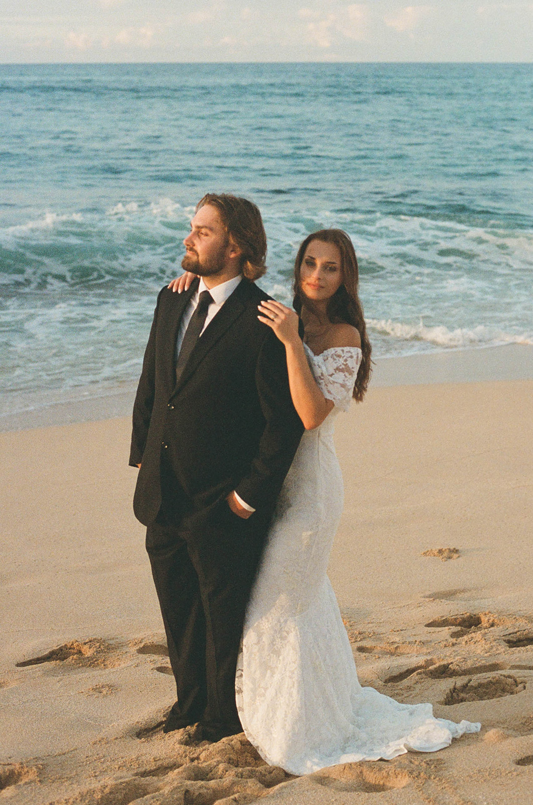 Bride resting her hand on the groom’s shoulder as they stand by the water, captured in a calm and intimate documentary wedding photography moment.