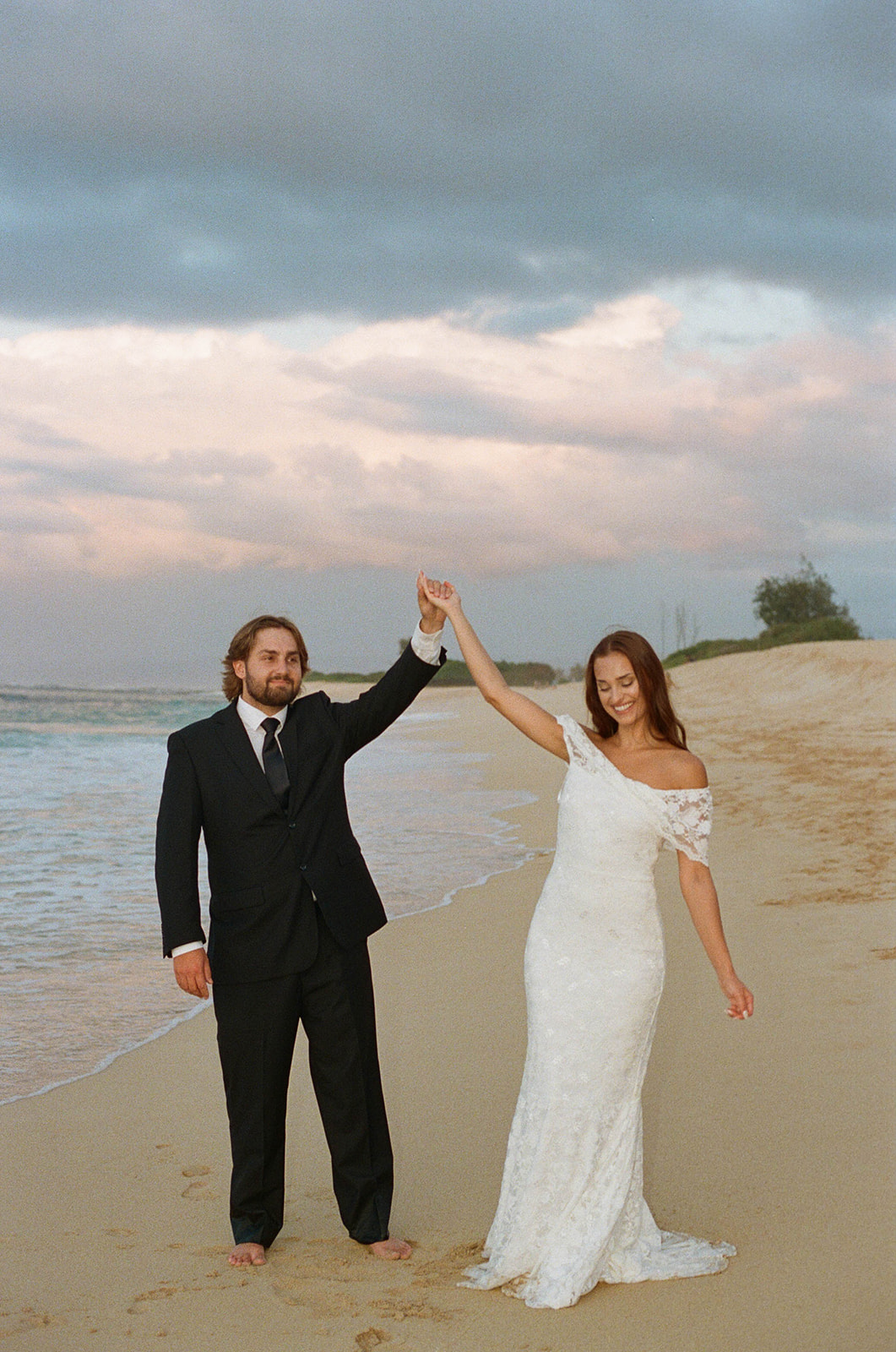 The bride and groom smiling and dancing on the beach during their sunrise photos during their Kauai wedding