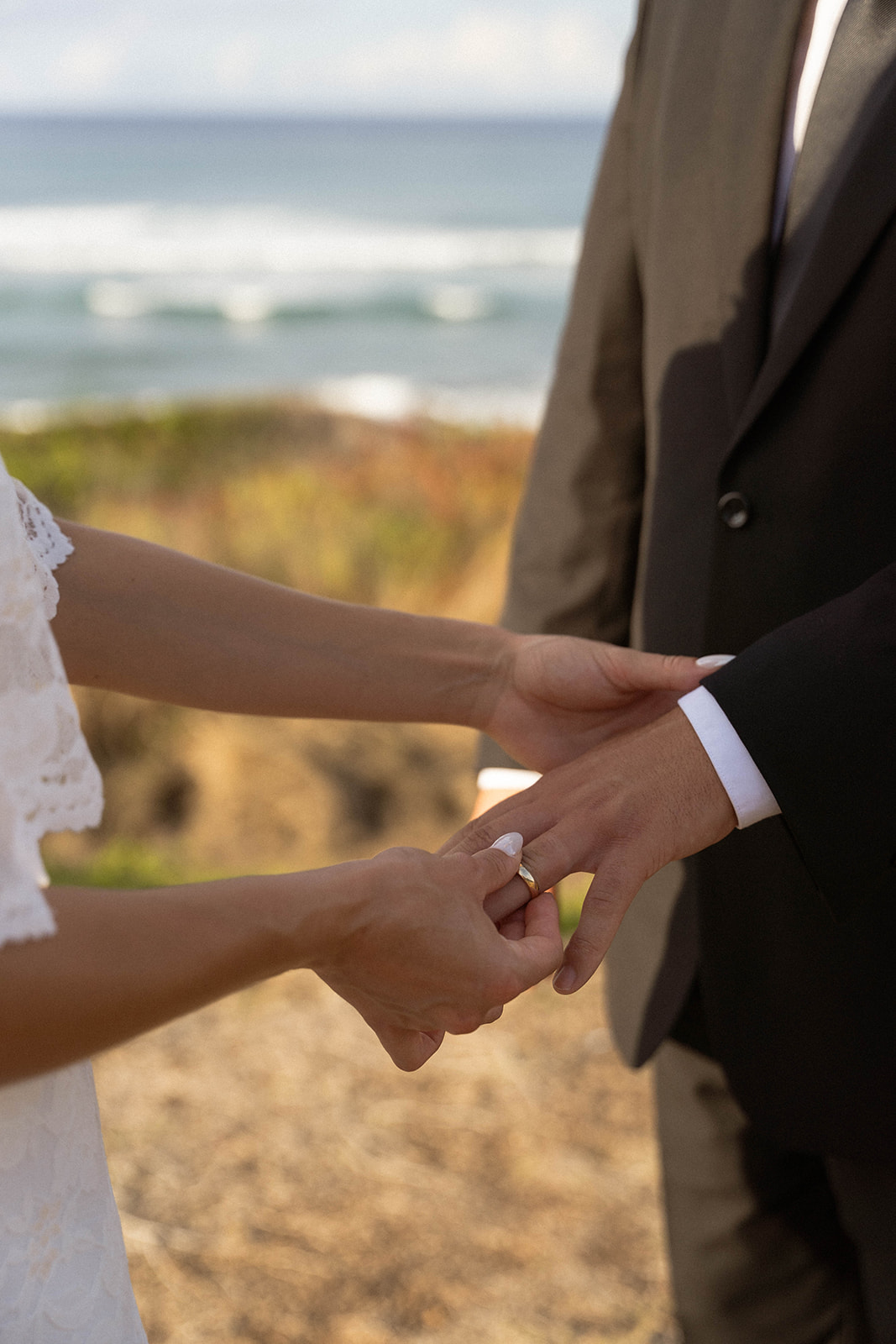 Close-up of the bride gently adjusting the groom’s wedding band during their intimate Kauai Wedding Planning ceremony on the coast.