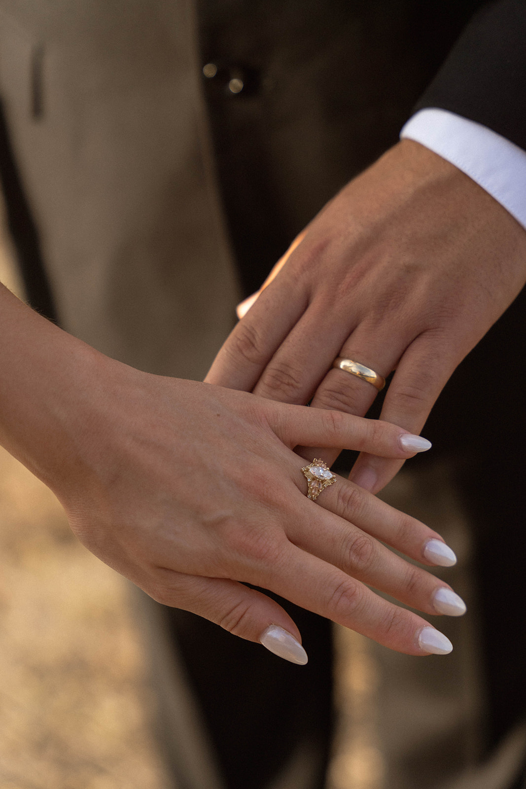 A close-up of two hands showing their wedding rings, the bride’s delicate oval ring resting above the groom’s classic gold band, documented in an intimate documentary wedding photography moment.