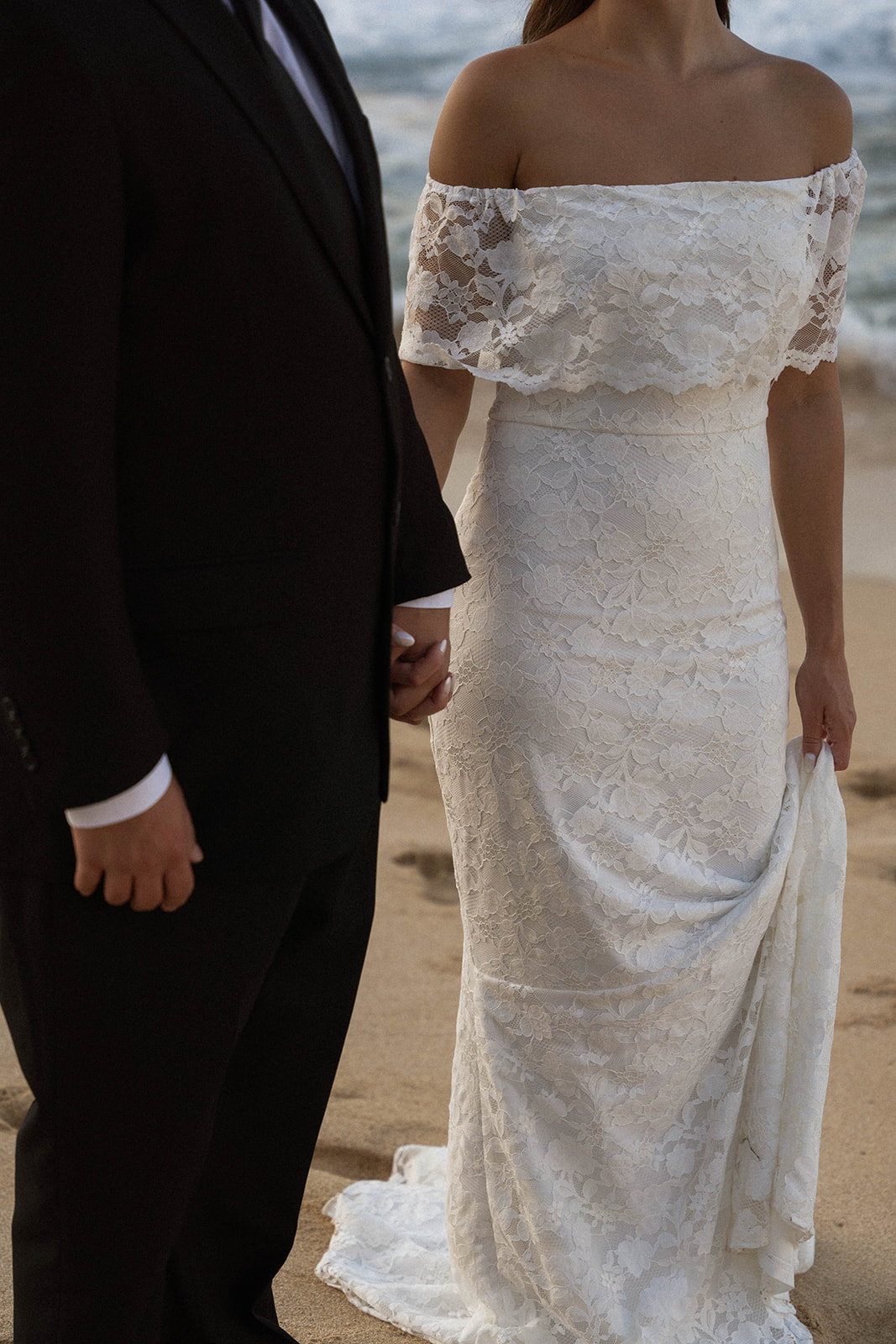 Close-up of the bride holding her lace dress while walking barefoot with the groom, focusing on texture and connection through documentary wedding photography.