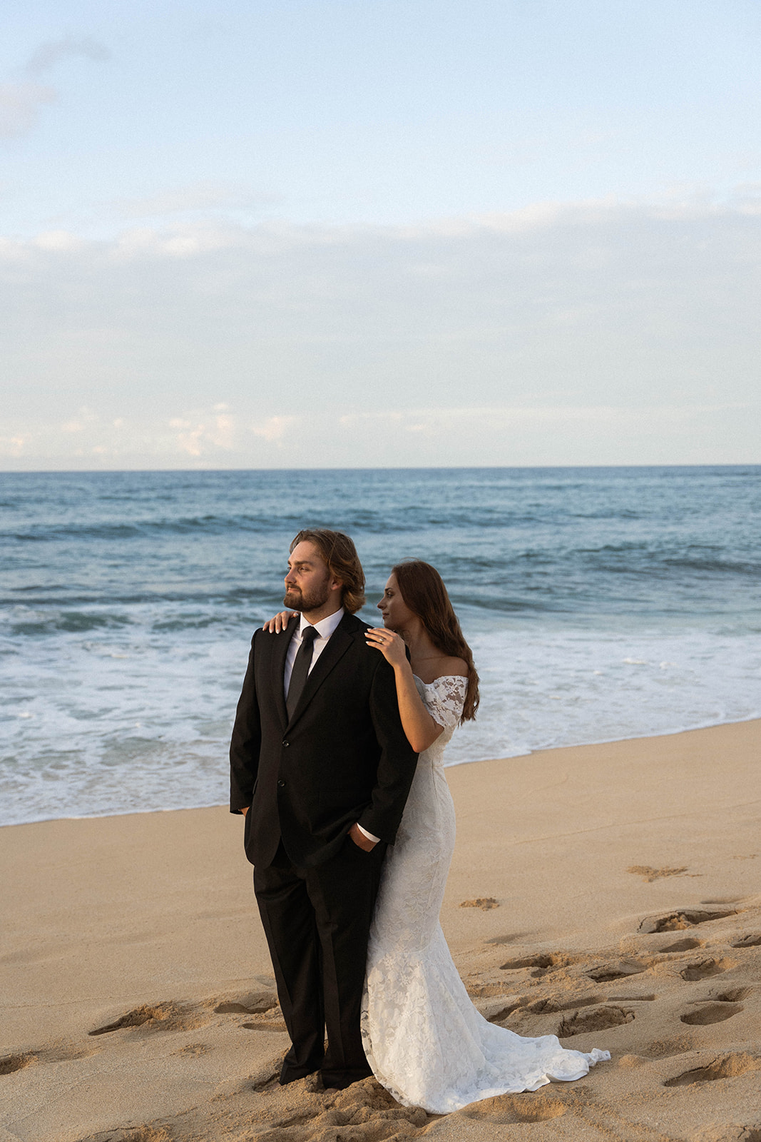 Bride resting her hand on the groom’s shoulder as they stand by the water, captured in a calm and intimate documentary wedding photography moment.