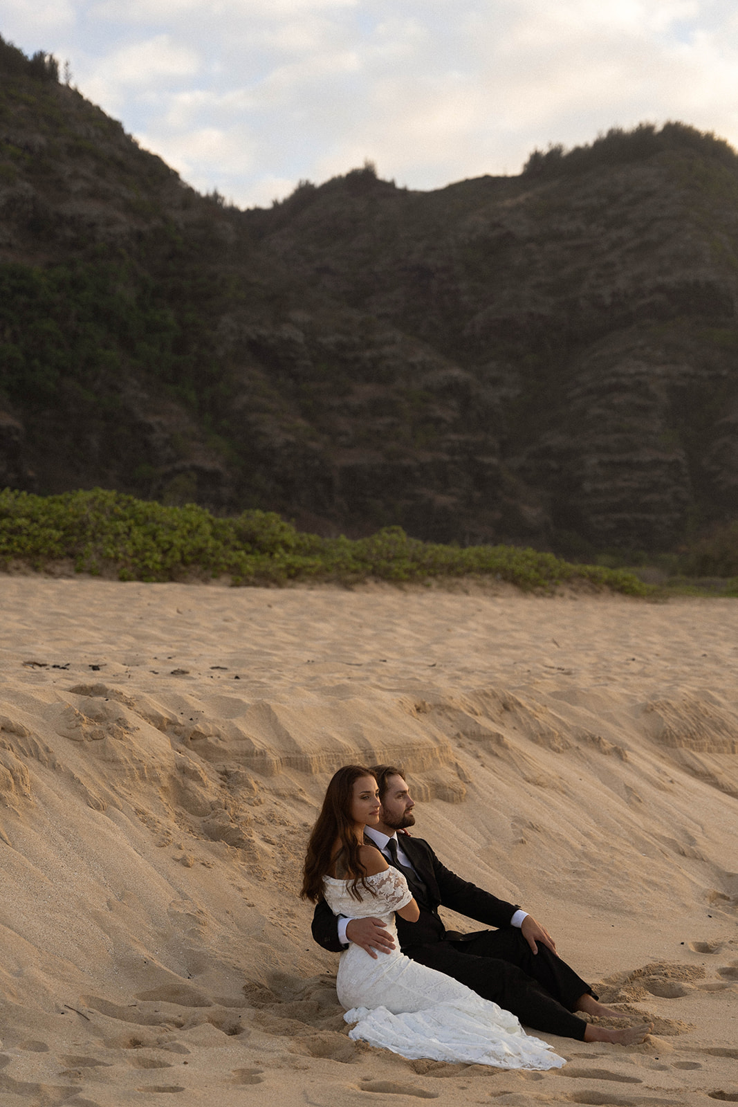 Couple sitting close together on a sandy dune overlooking the ocean, captured during their intimate Kauai Wedding Planning session photos.
