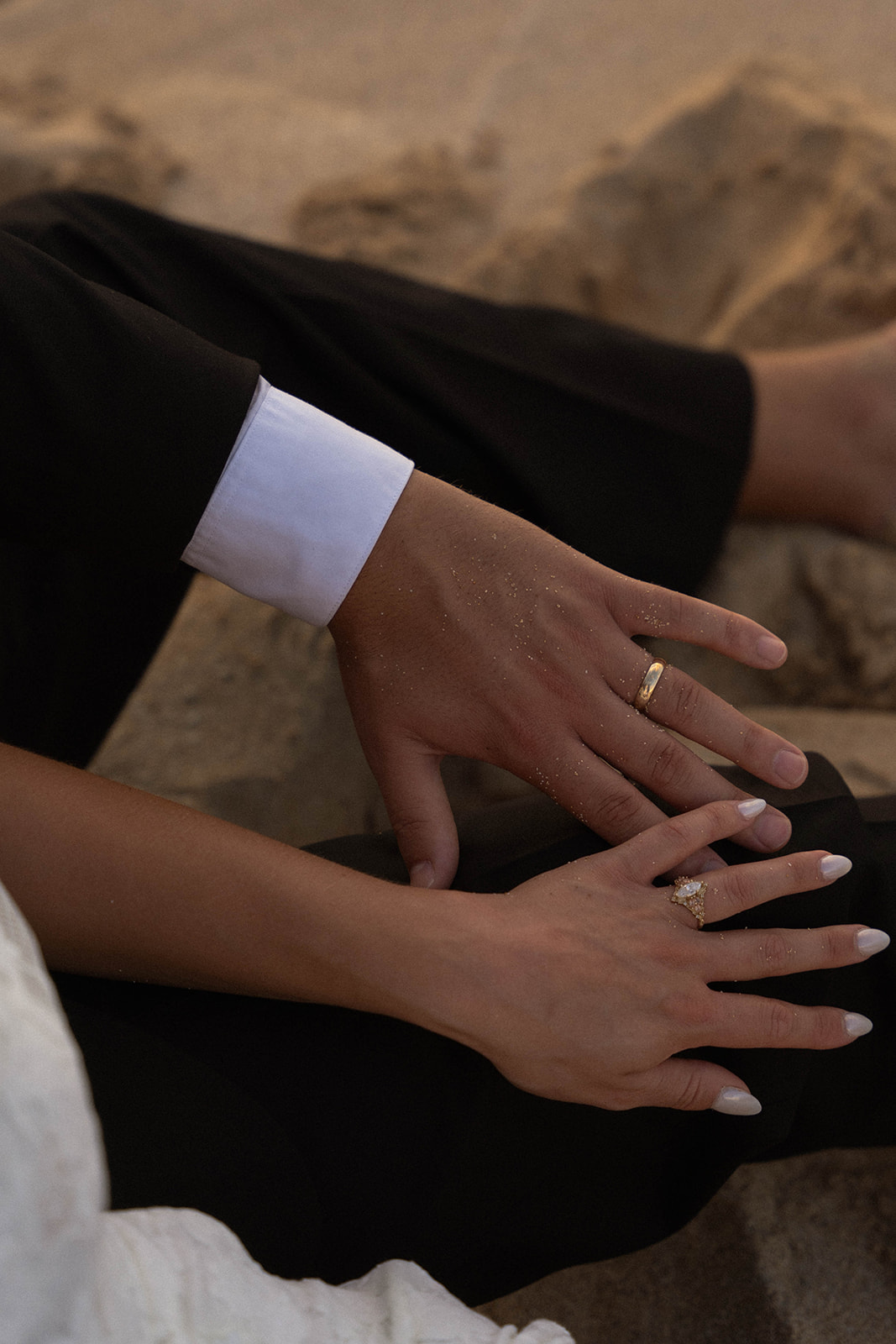 Close-up of the couple’s hands resting together in the sand, featuring their wedding bands during a romantic Kauai Wedding beach moment.