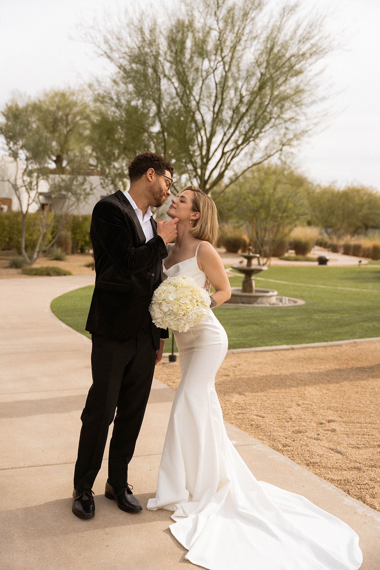 Bride and groom sharing a playful moment outdoors, the bride holding a white bouquet.