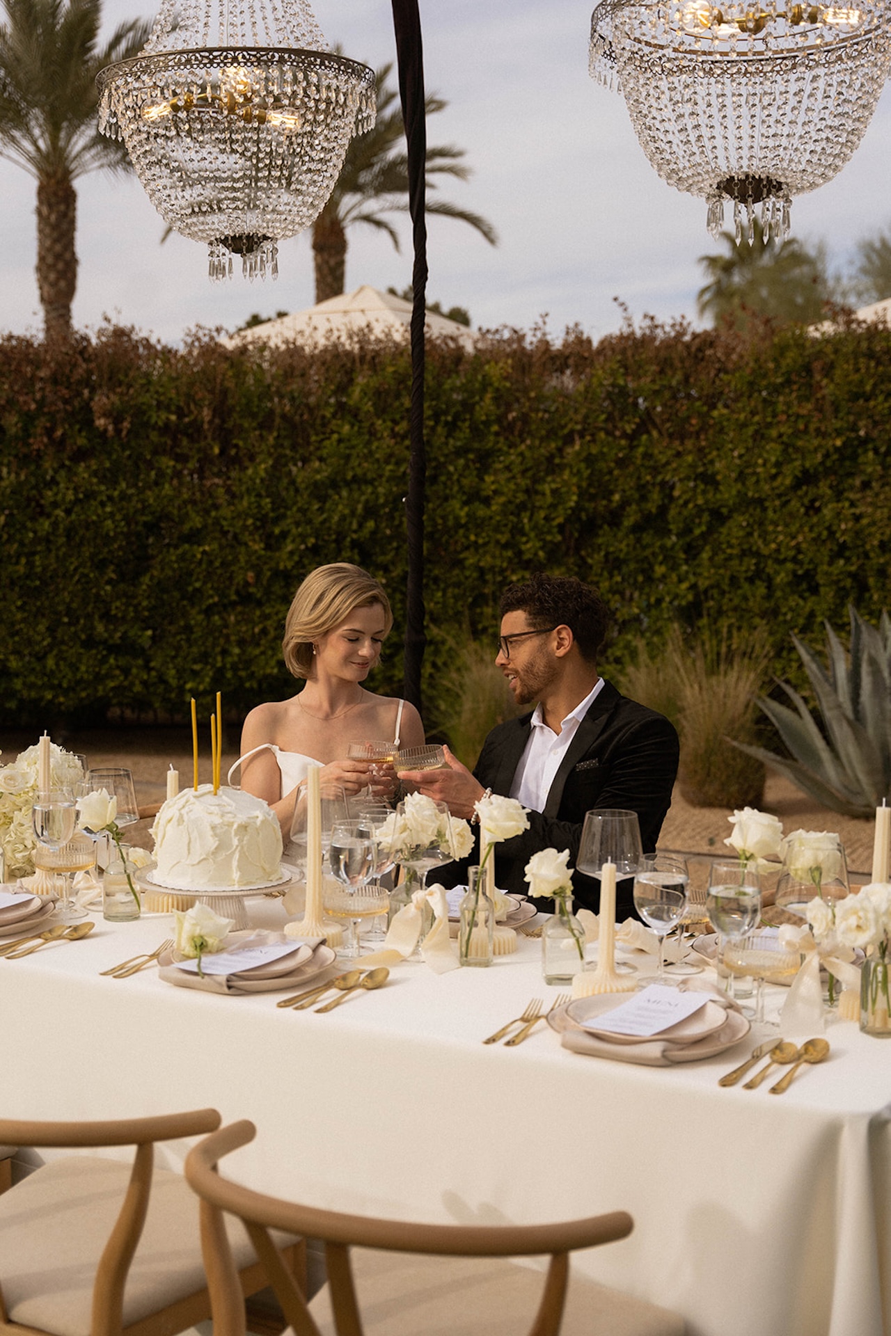 Romantic dinner setting beneath hanging chandeliers, captured at sunset at a luxury wedding venue.
