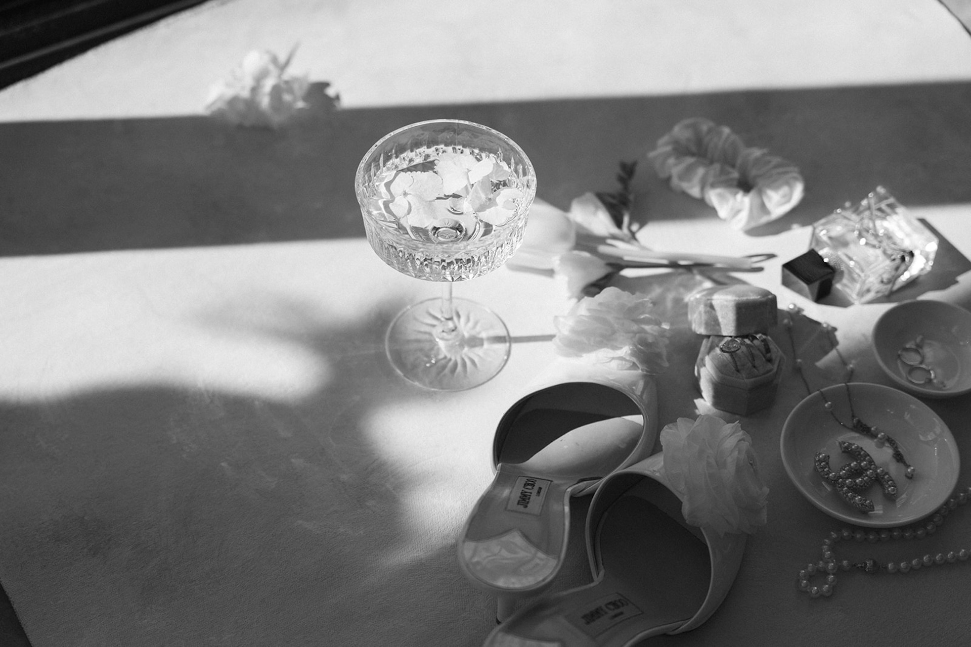 Flat lay of champagne glass, shoes, and accessories styled in soft sunlight at a luxury wedding venue.
