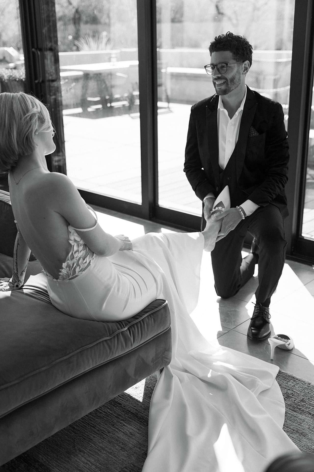 Groom kneeling as he helps bride with her heels, sharing a quiet pre-ceremony moment.