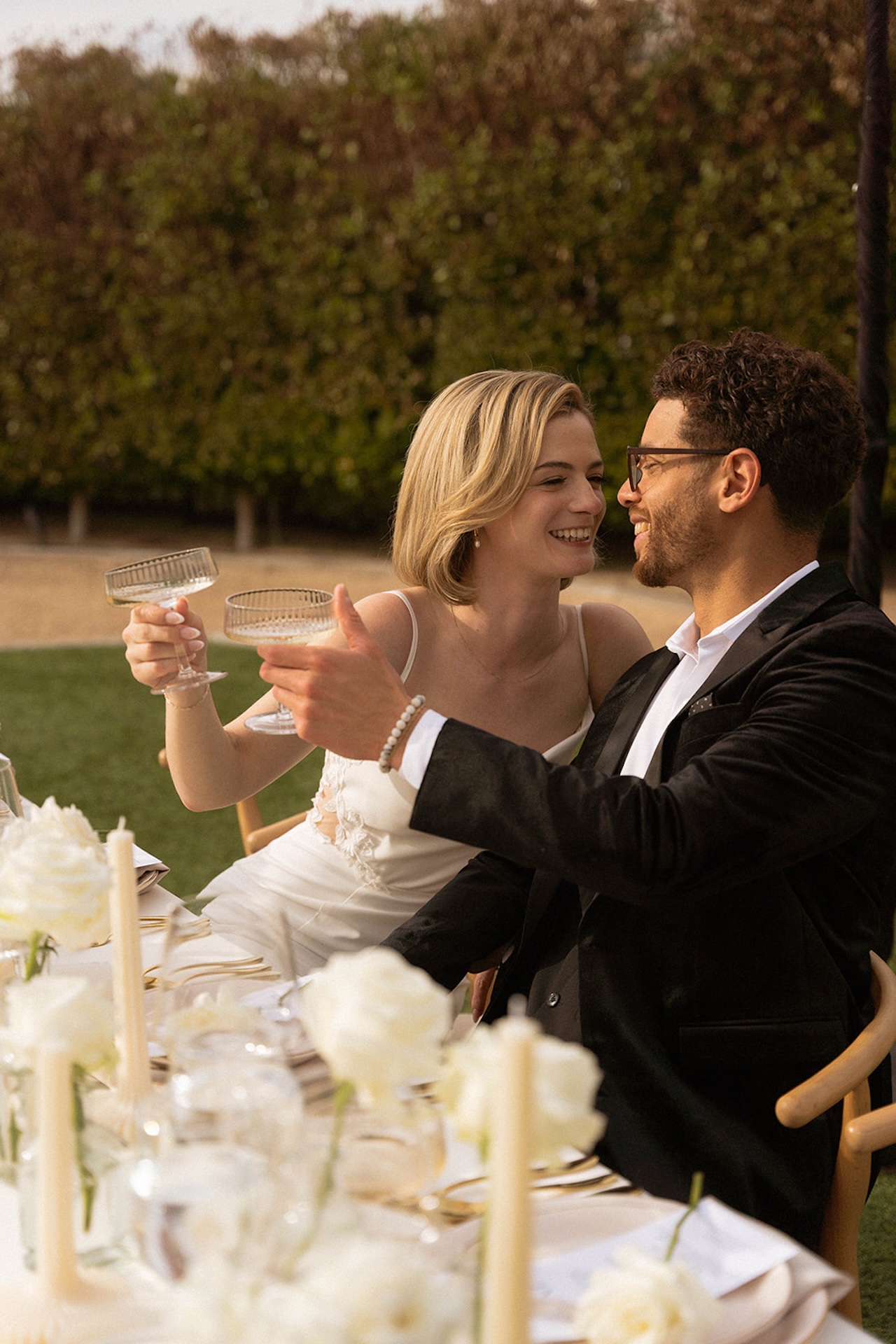 Bride and groom toasting at a candlelit reception table, smiling together.