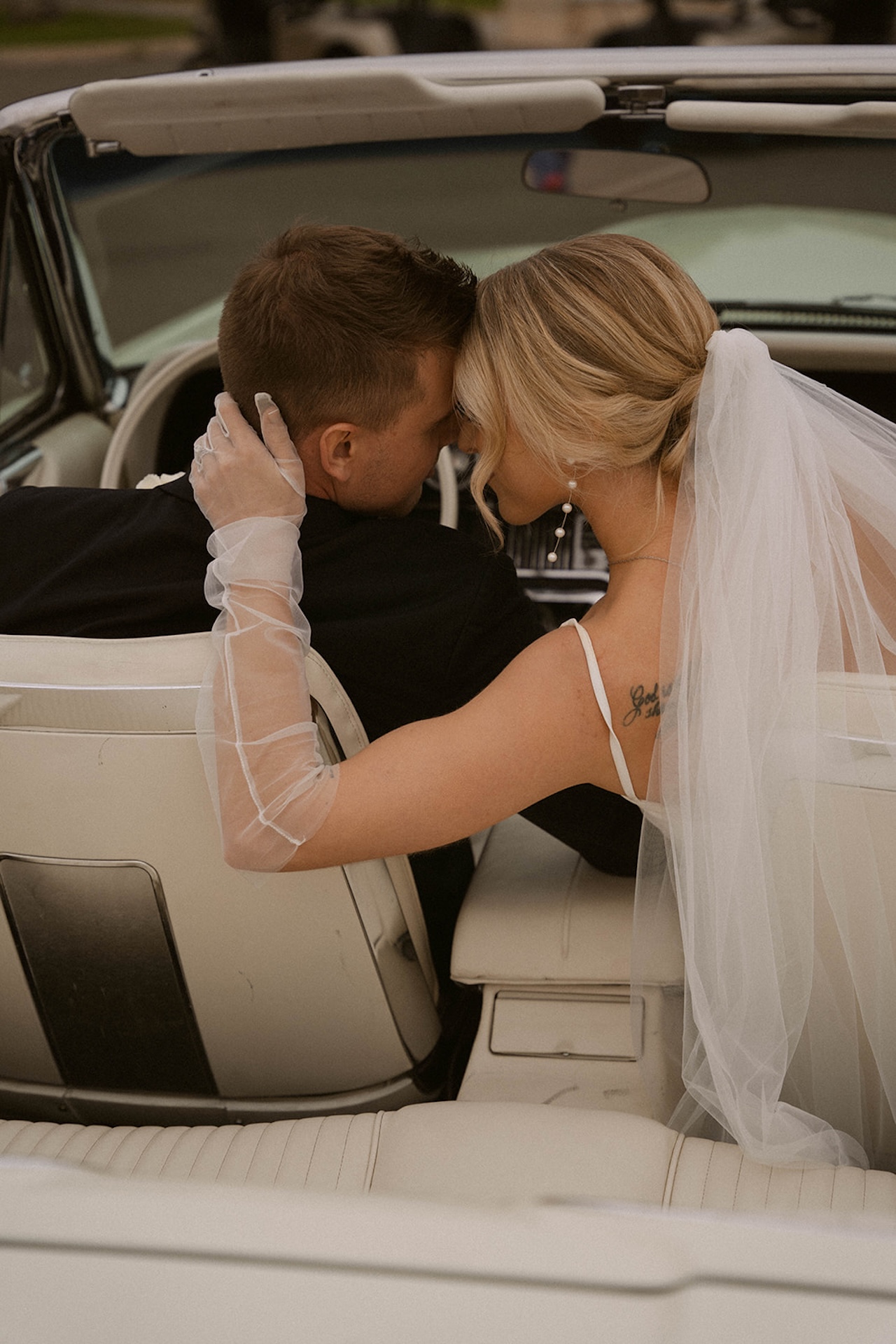 Bride holding her groom close while sitting together in a white convertible during their intimate wedding.