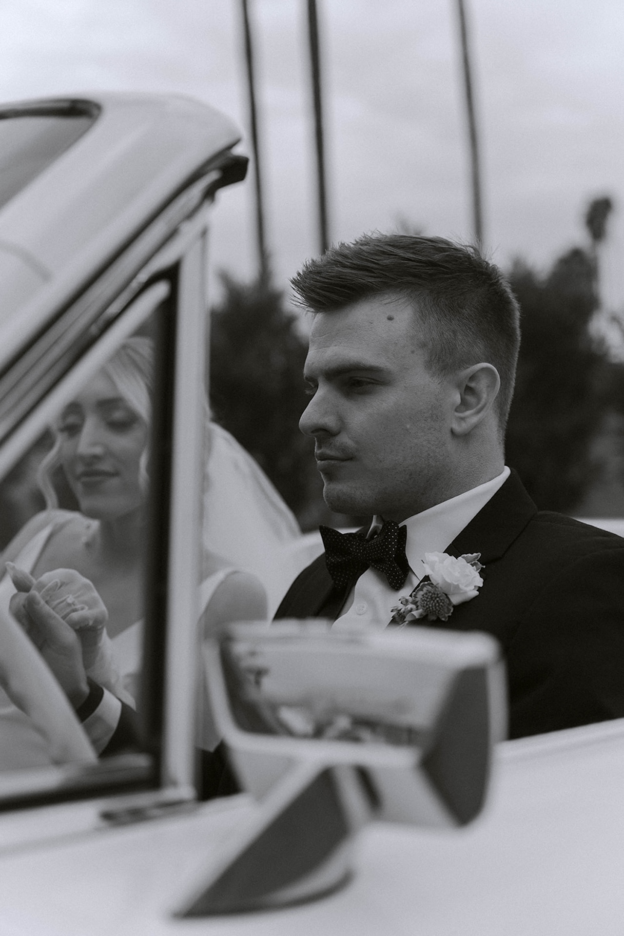 Groom sitting in a vintage car with the bride beside him.