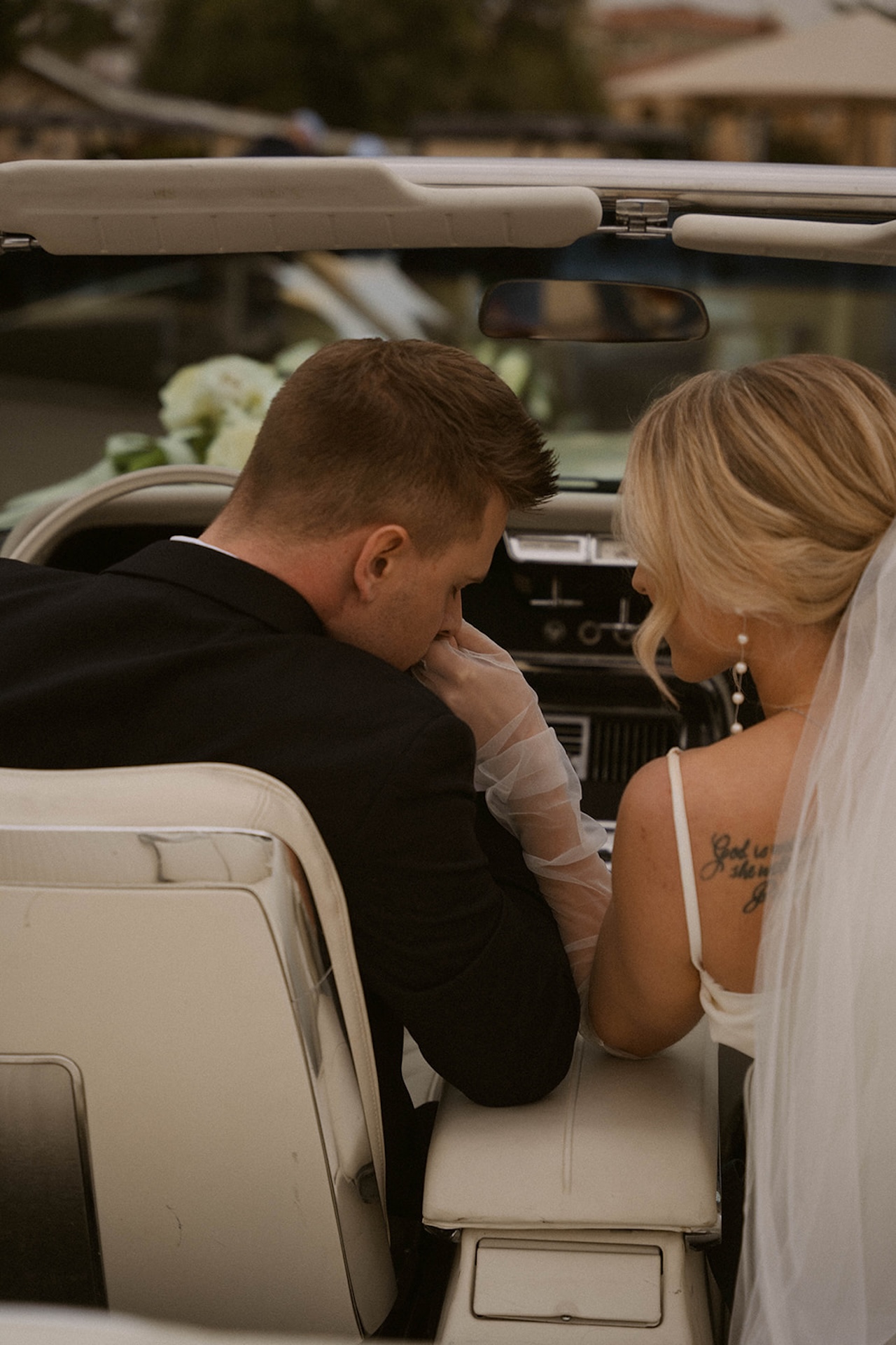 The groom kissing the brides hand as they sit in the front seat of a convertable during their intimate wedding bride and groom portraits.