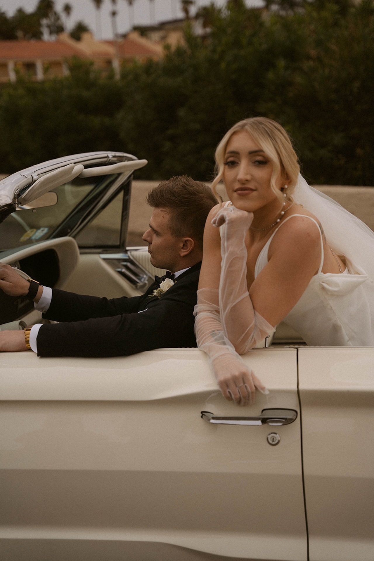 Bride leaning on the seat behind the groom as he sits in the front seat of their convertable during their intimate wedding photos.