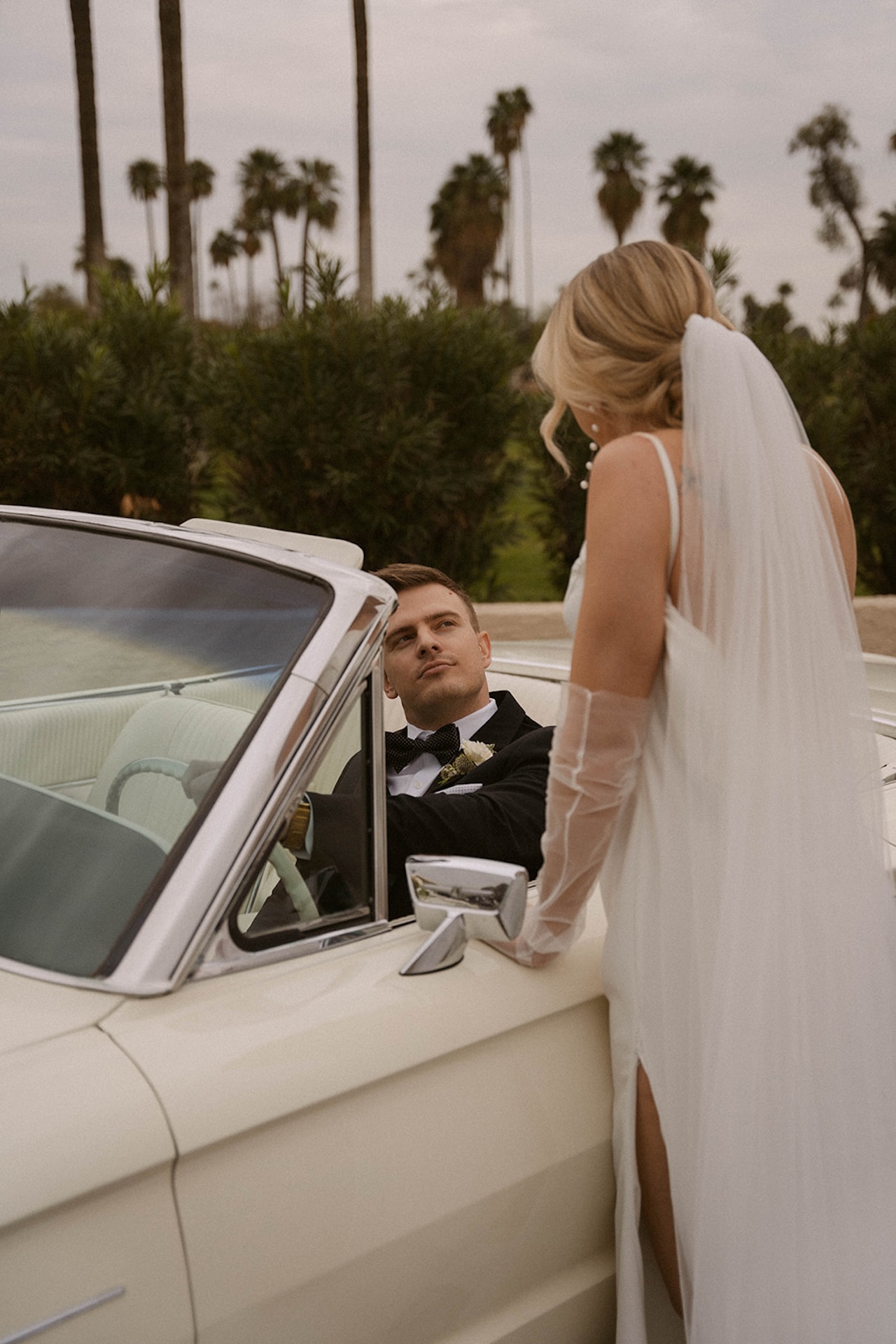 Groom looking up at his bride as she stands beside the car during their intimate wedding portraits.