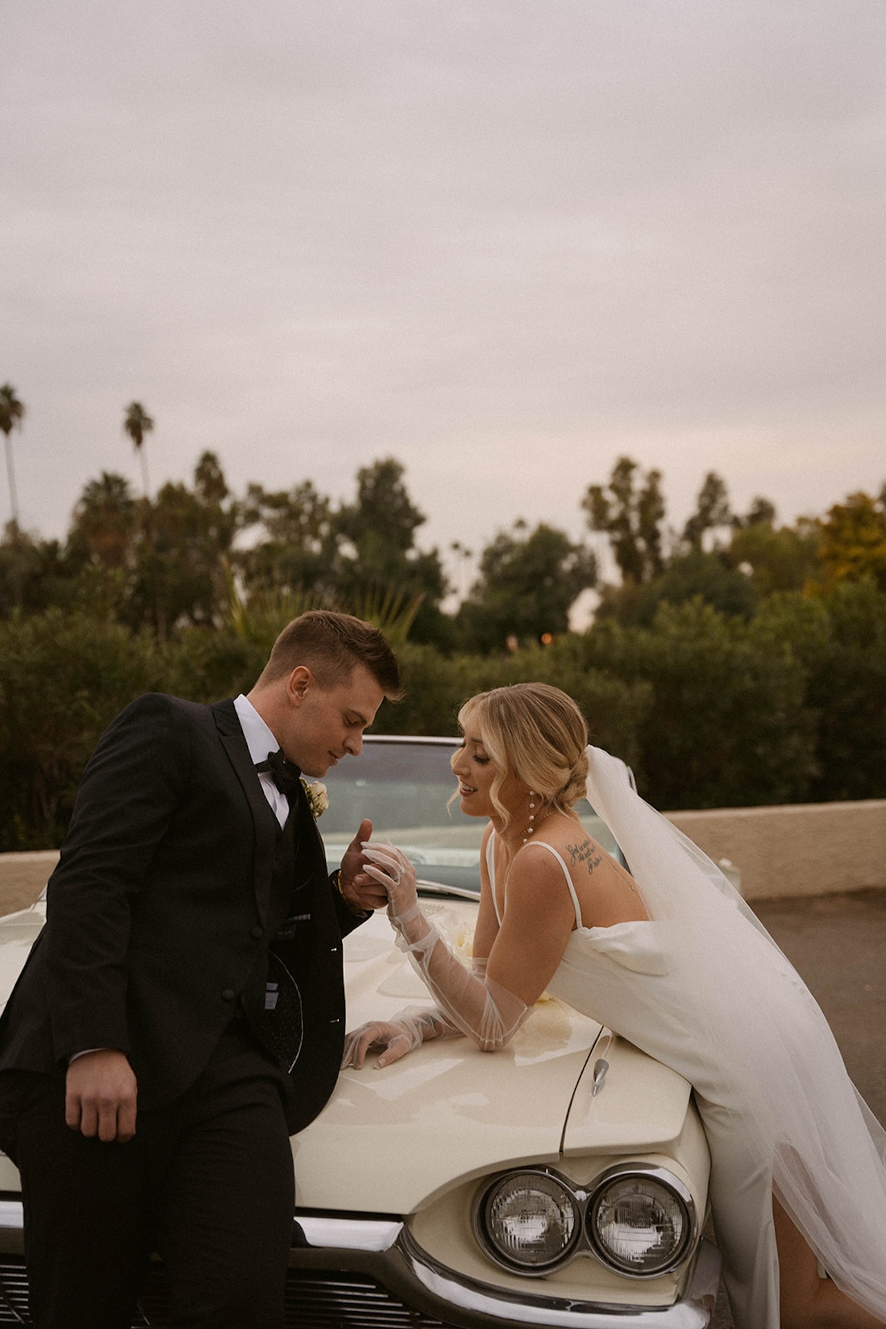 Bride and groom leaning over the hood of the convertable holding hands and chatting during their intimate wedding.