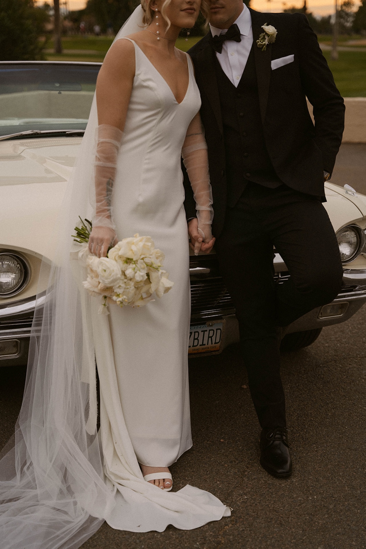 Bride holding her bouquet while standing beside her groom in front of a vintage car.
