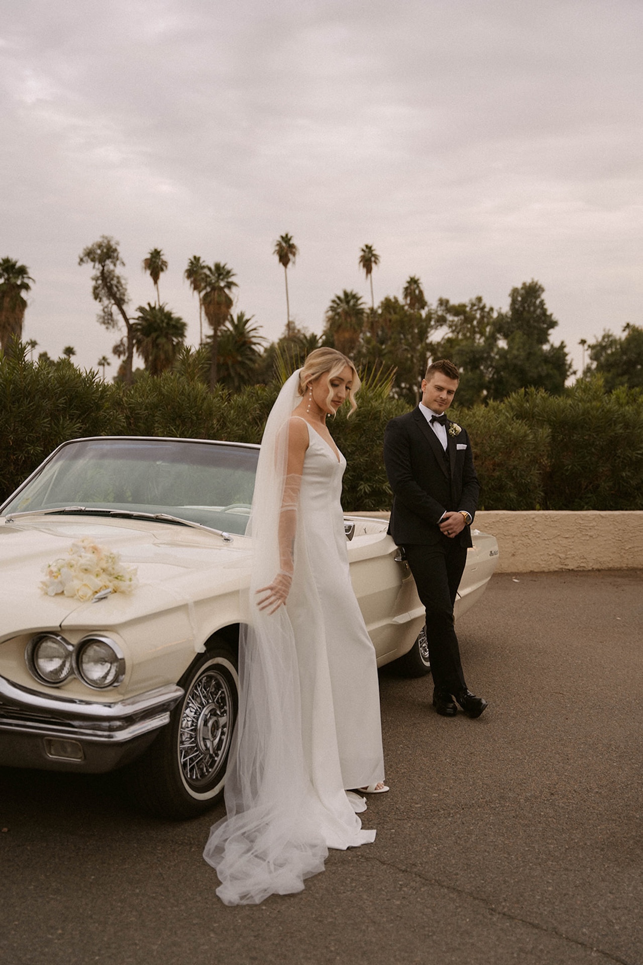 Bride walking beside a convertible as her groom looks at her lovingly during their intimate wedding.