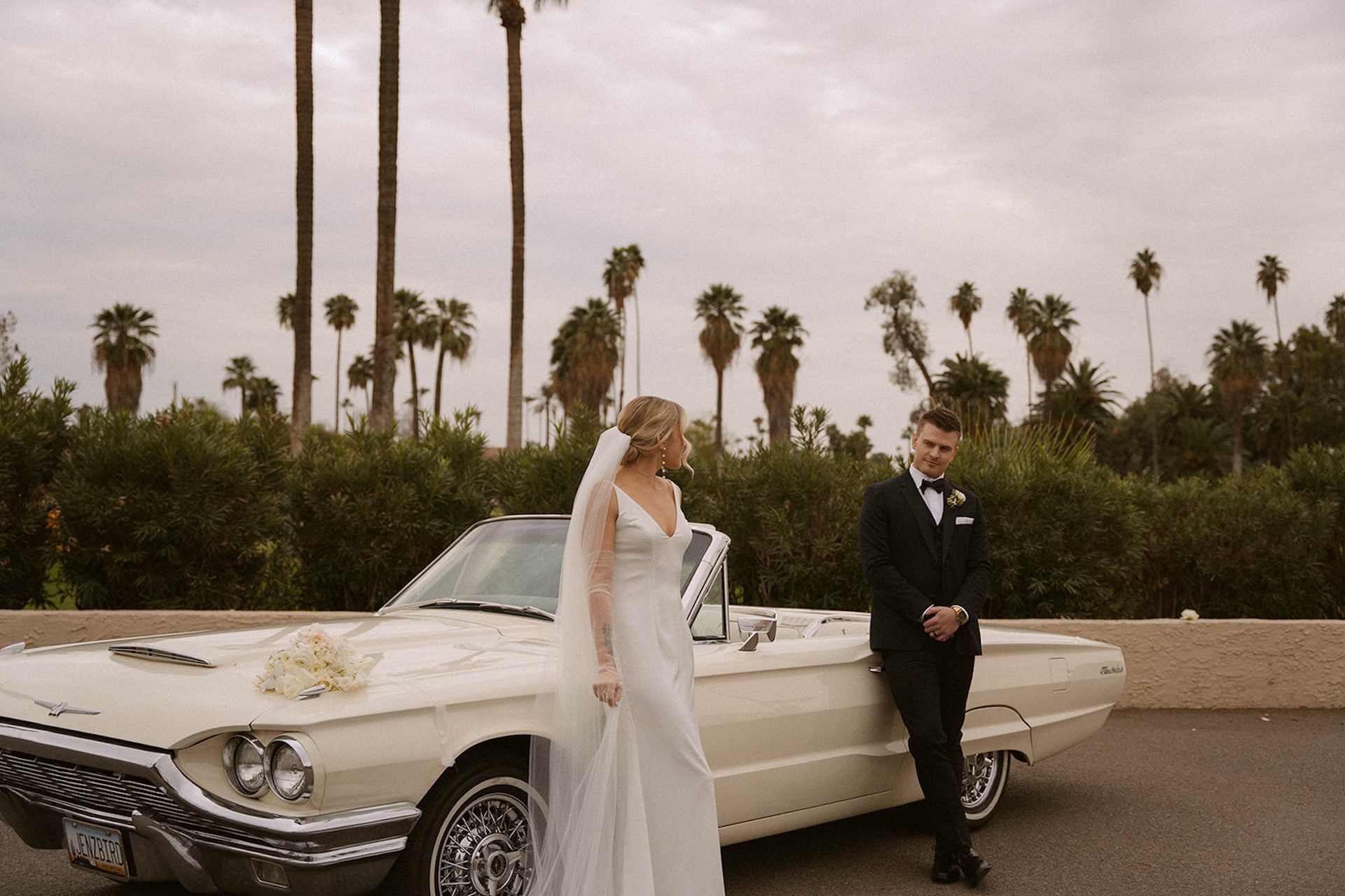 Bride walking beside a convertible as her groom looks at her lovingly during their intimate wedding.