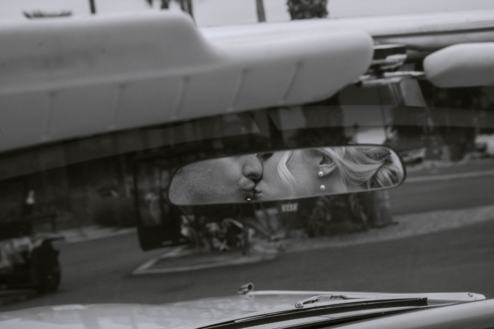A classy black and white image of the bride and groom kissing in the front seat of a convertable through the rear view mirror.