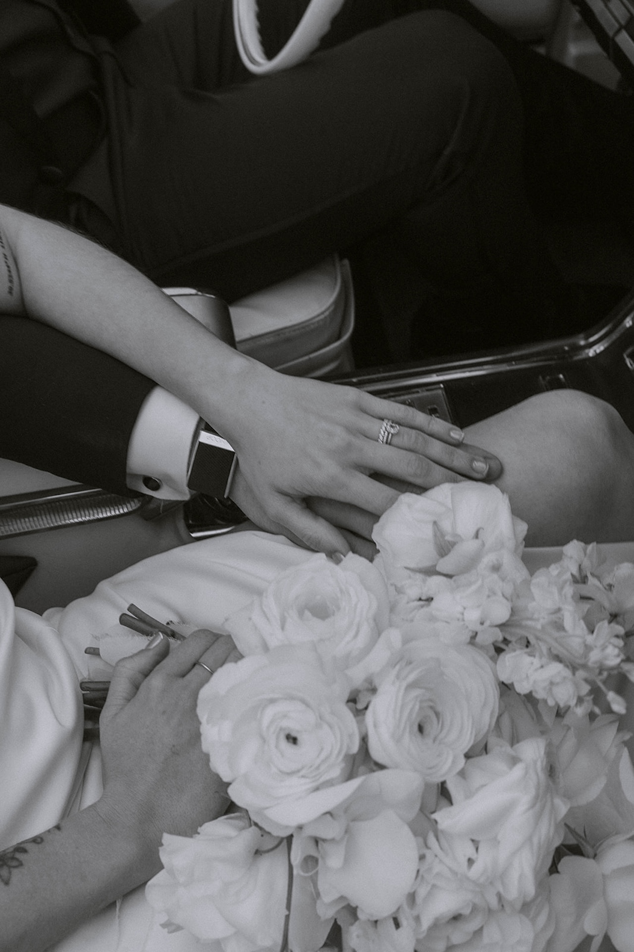 Black and white detail photo of the bride and groom holding hands in her lap during their intimate wedding bride and groom portraits