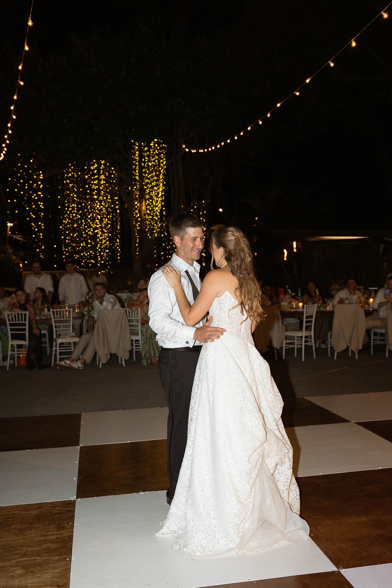 The couple sharing their first dance under string lights during an outdoor evening reception. Inspiration for Big Island Wedding Planning.