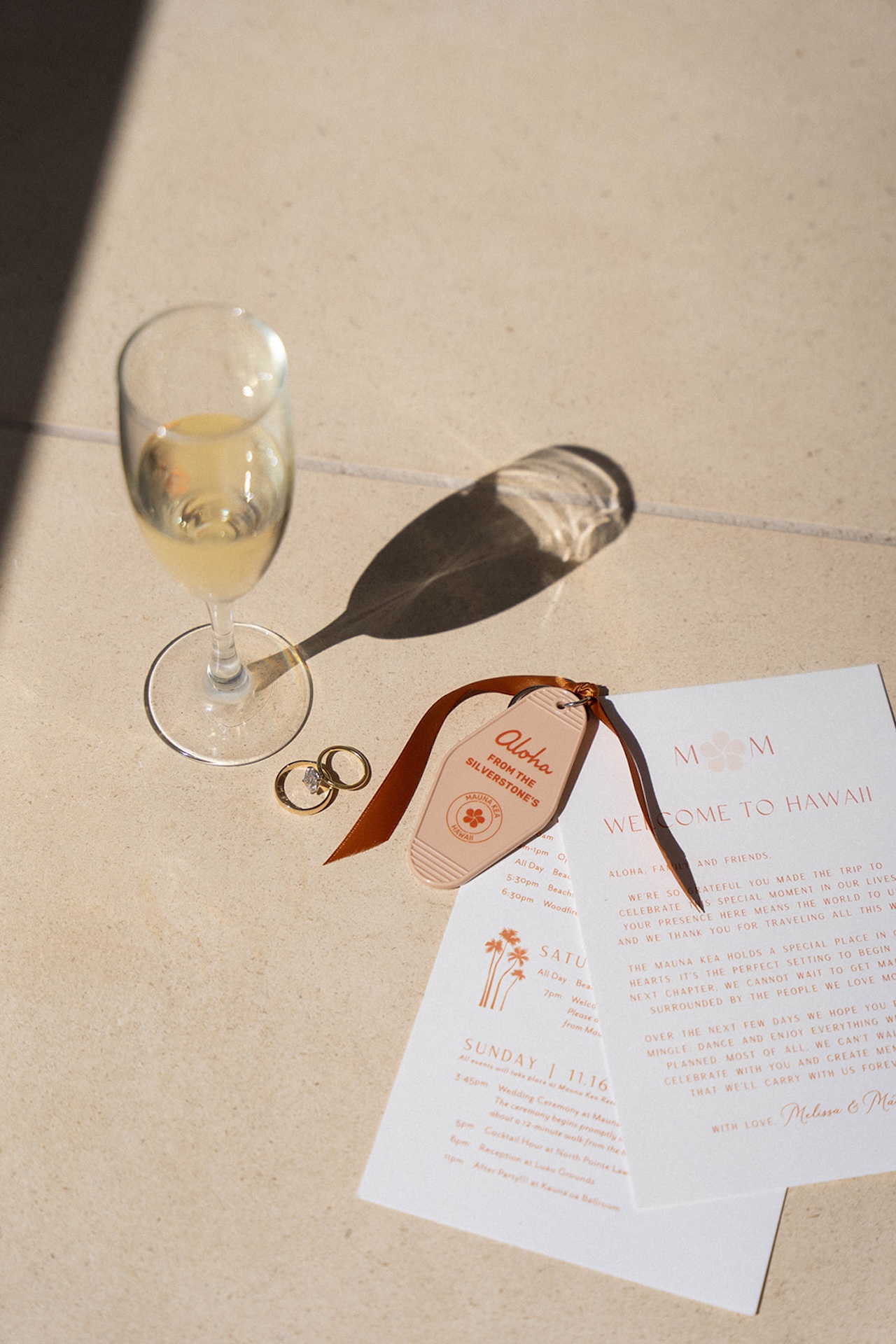Flat lay of wedding details including rings, welcome cards, and a champagne glass styled in soft neutral tones.