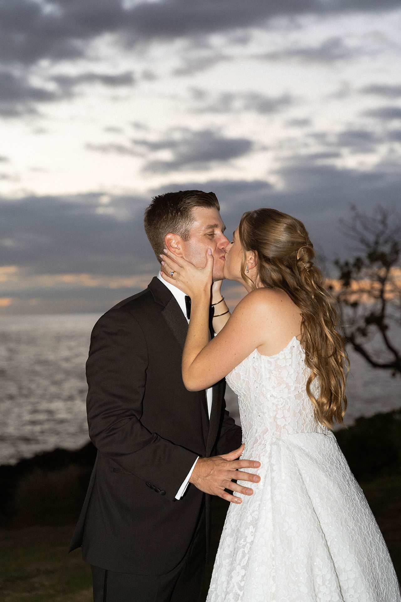 The couple shares an intimate kiss at sunset with the ocean behind them, highlighting the romantic atmosphere of big island wedding planning.