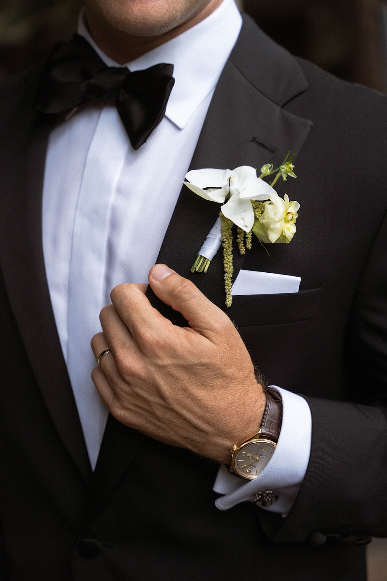 Close-up of the groom’s tuxedo details including a white boutonniere, bow tie, and classic wristwatch.