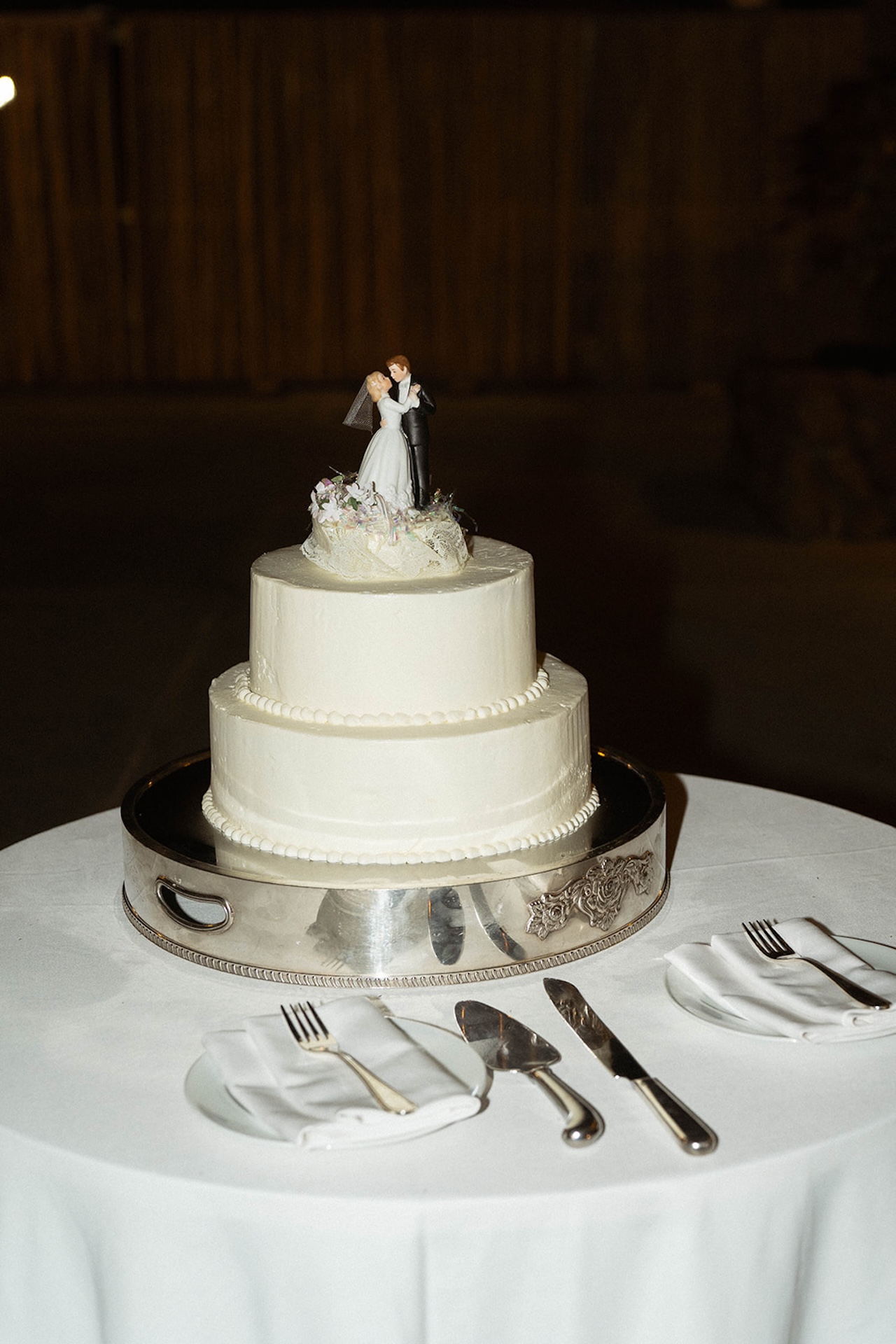 A classic white wedding cake with a figurine topper displayed on a reception table.