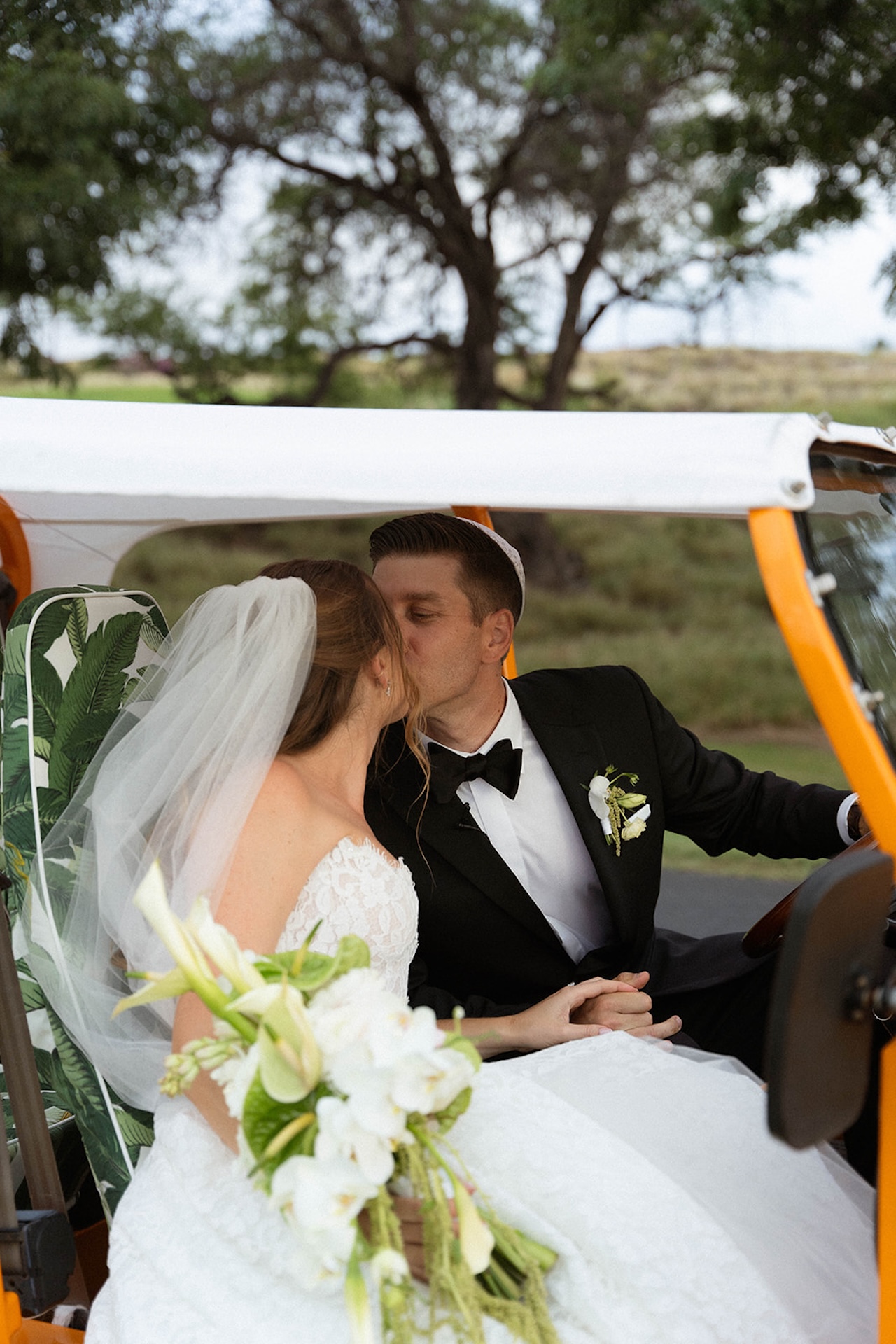 The bride and groom sharing a quiet kiss while seated together in a vintage getaway vehicle. Inspiration for Big Island Wedding Planning