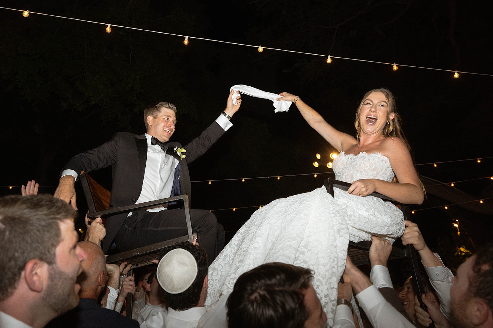 The bride and groom lifted in chairs during a lively nighttime wedding reception celebration