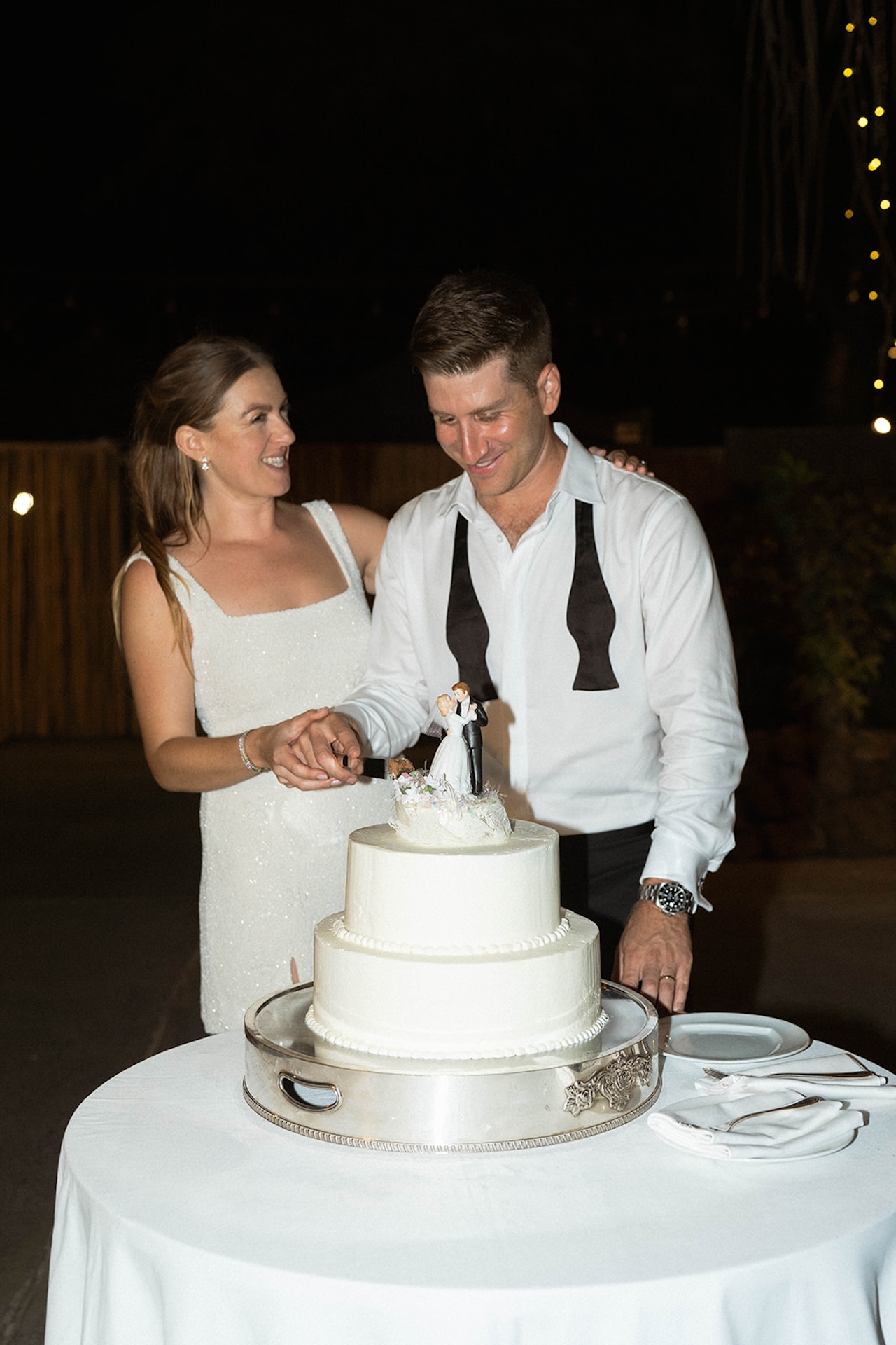 A flash photo of the bride and groom cutting into their simple and elegant white wedding cake.