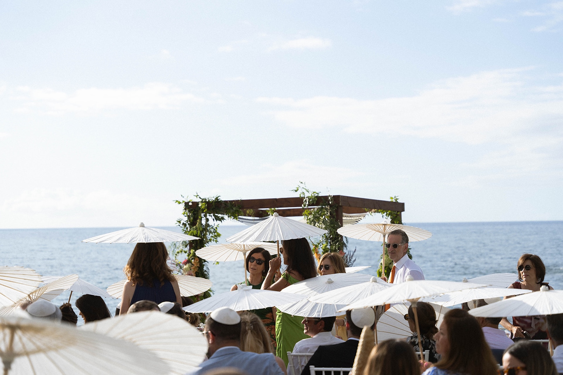 Guests holding white parasols while seated at a seaside wedding ceremony. Perfect for inspiration for Big Island Wedding Planning