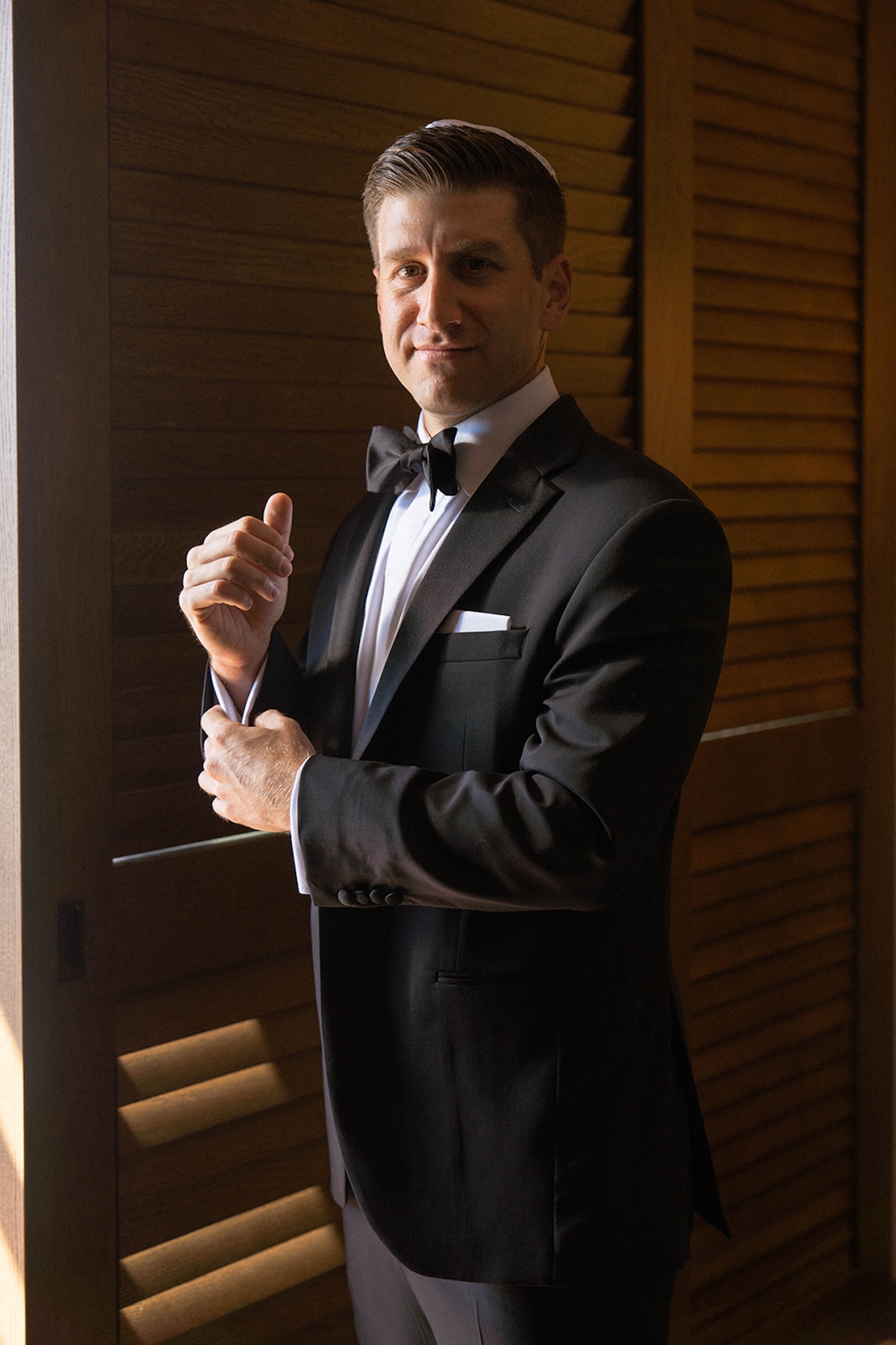 The groom adjusts his cufflinks in soft window light, a quiet getting ready moment during big island wedding planning.