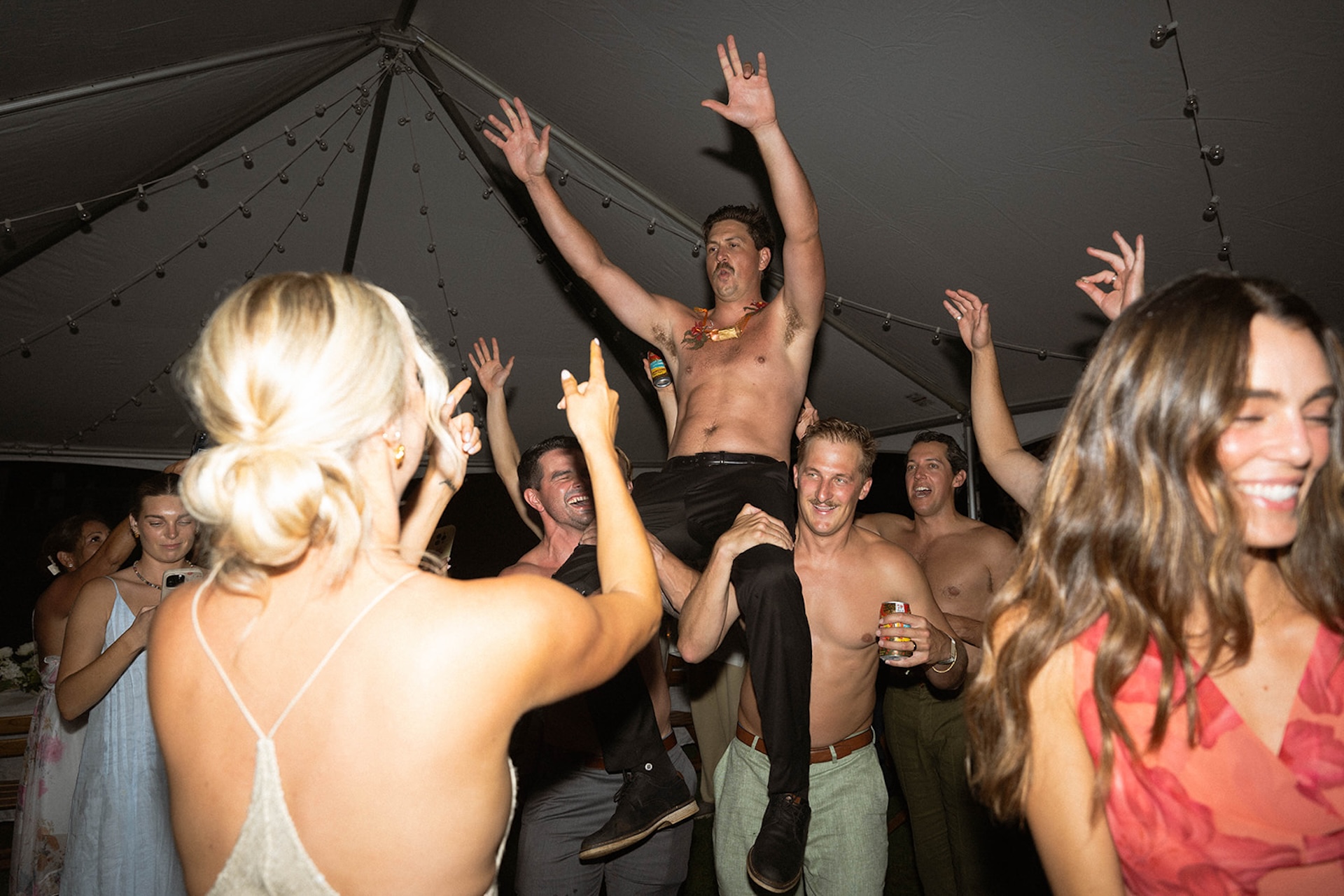 A high-energy dance floor moment as friends lift the groom into the air beneath a tent at one of the most lively Kauai wedding venues.