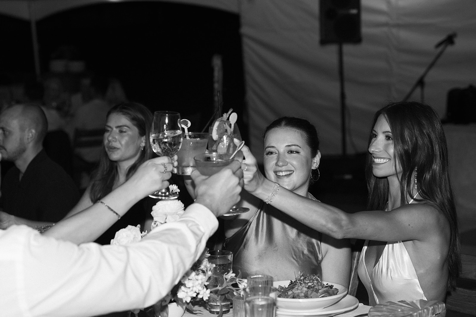 A group of friends clink cocktails and wine glasses during dinner at one of the most intimate Kauai wedding venues.