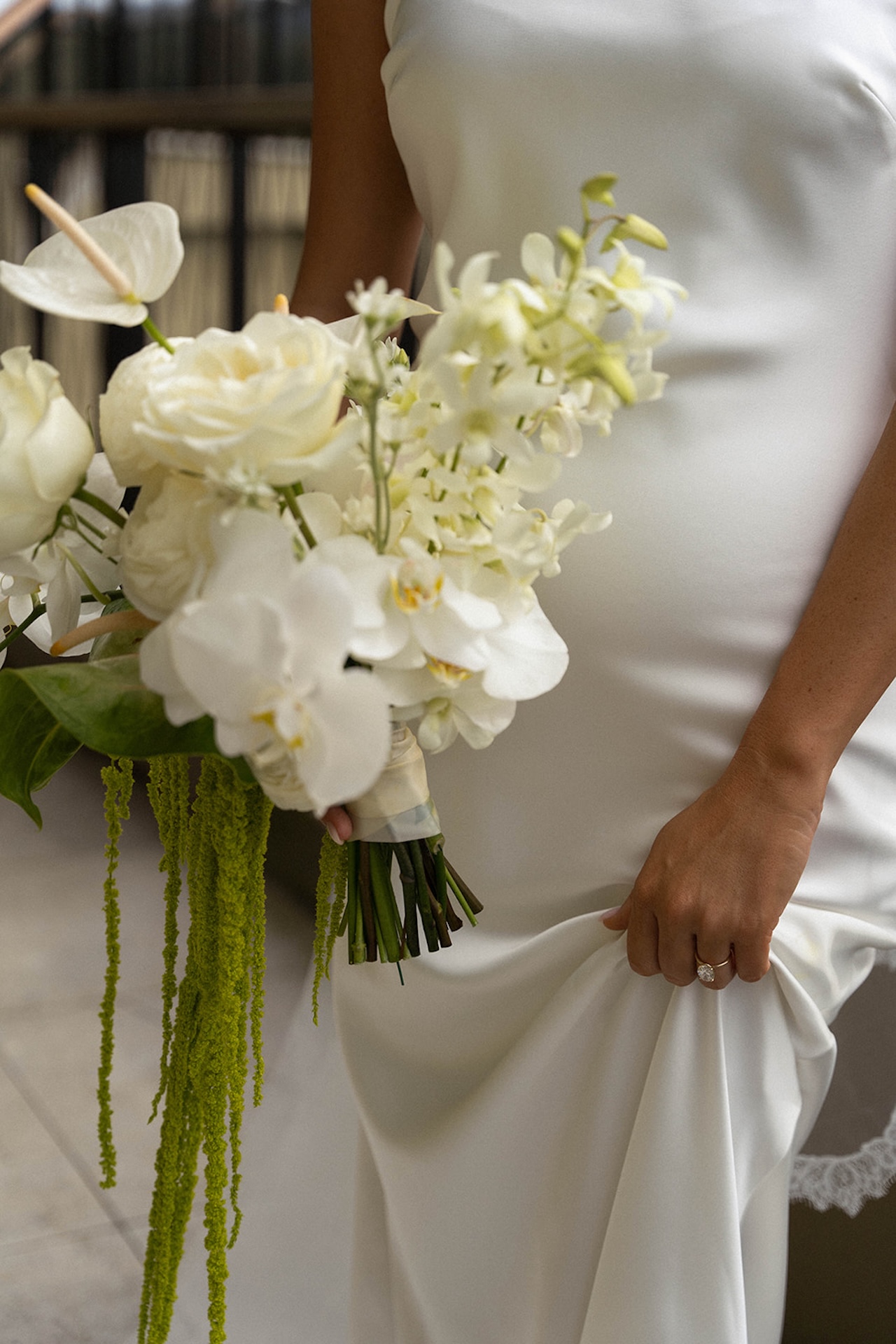 Close-up of a bride holding a cascading white orchid bouquet, highlighting minimalist bridal style and elegant floral details.
