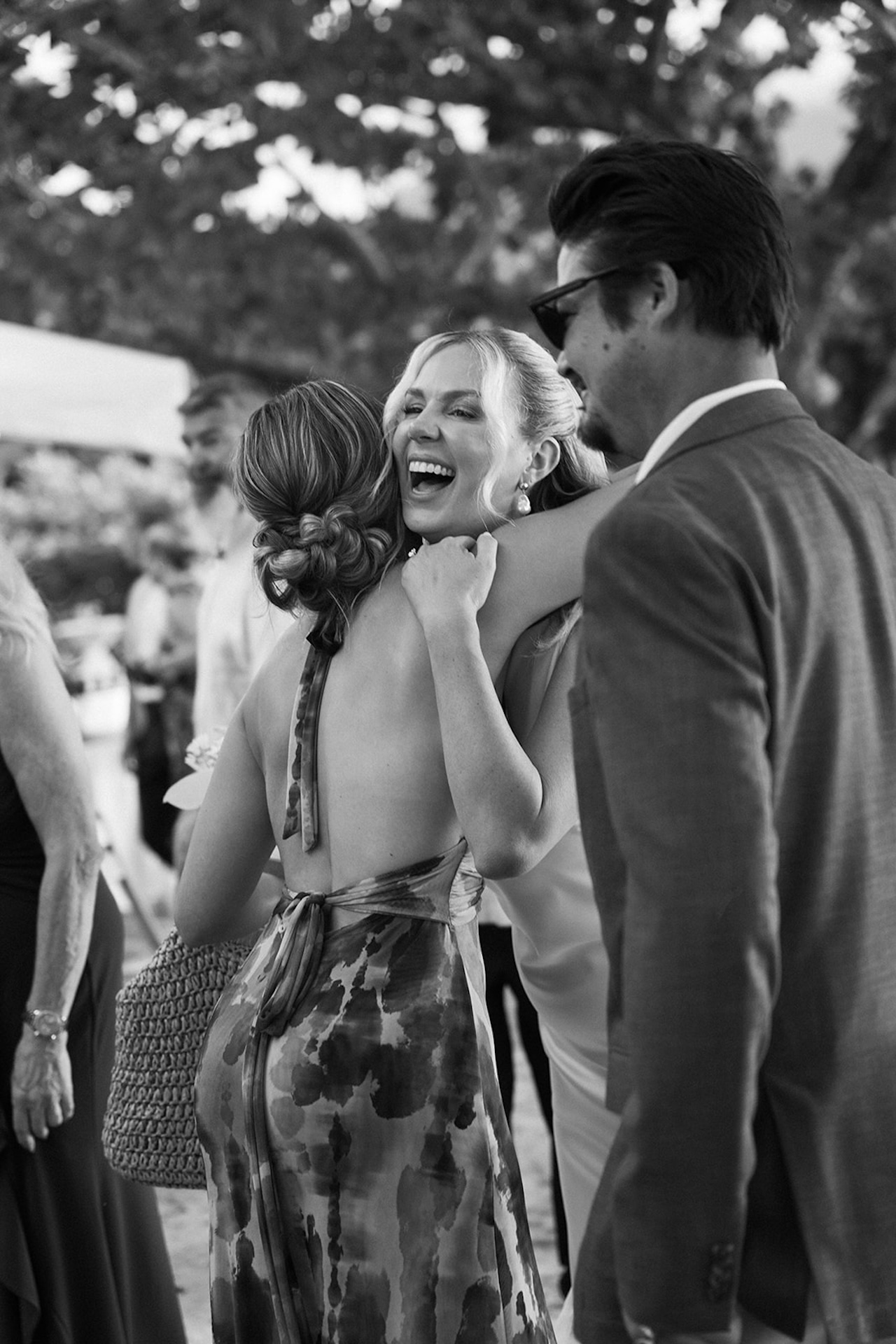 A joyful candid moment as guests embrace and laugh during an outdoor celebration beneath trees at one of the most welcoming Kauai wedding venues.