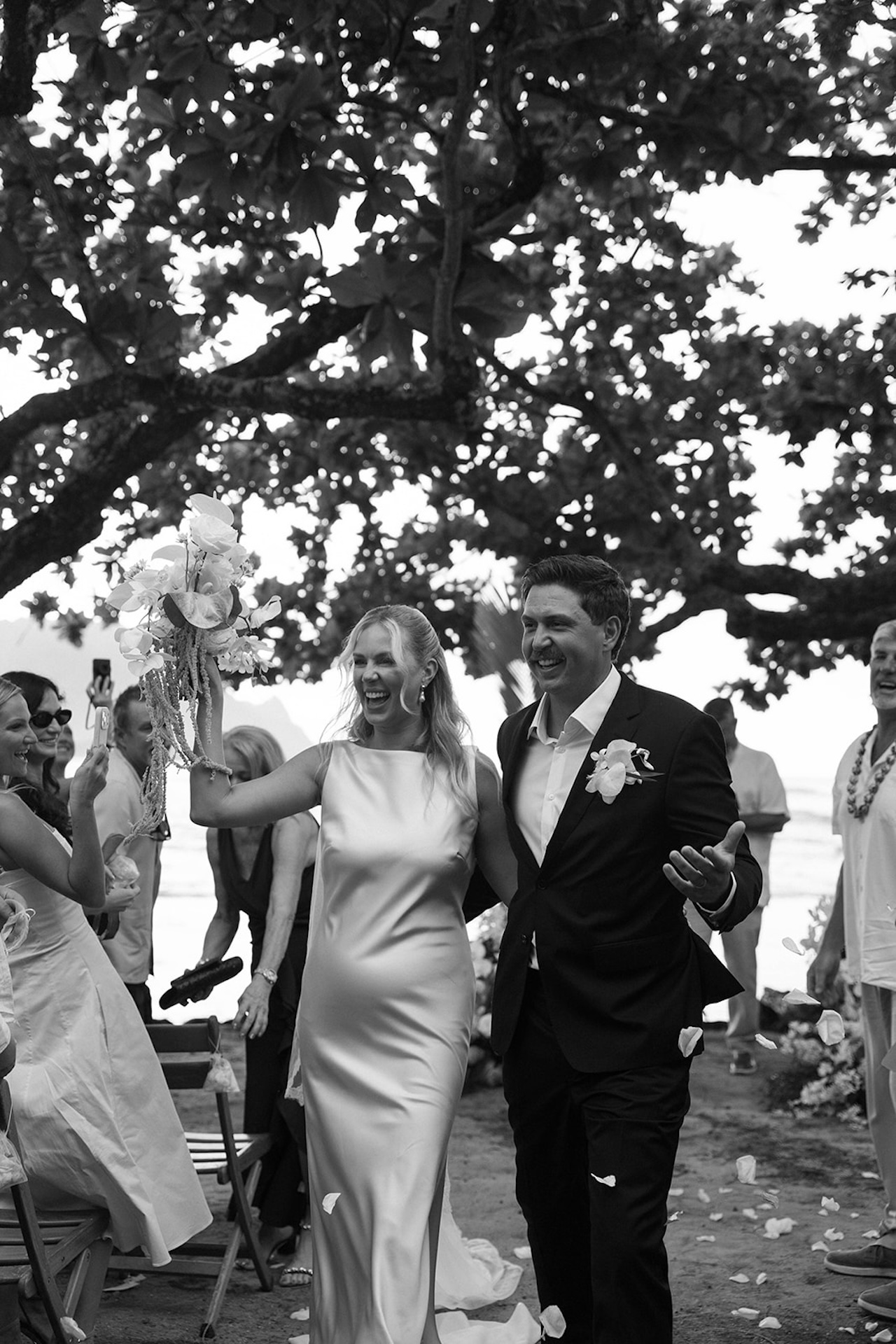 The newly married couple walks down the aisle together as guests cheer and toss petals at one of the most joyful Kauai wedding venues.