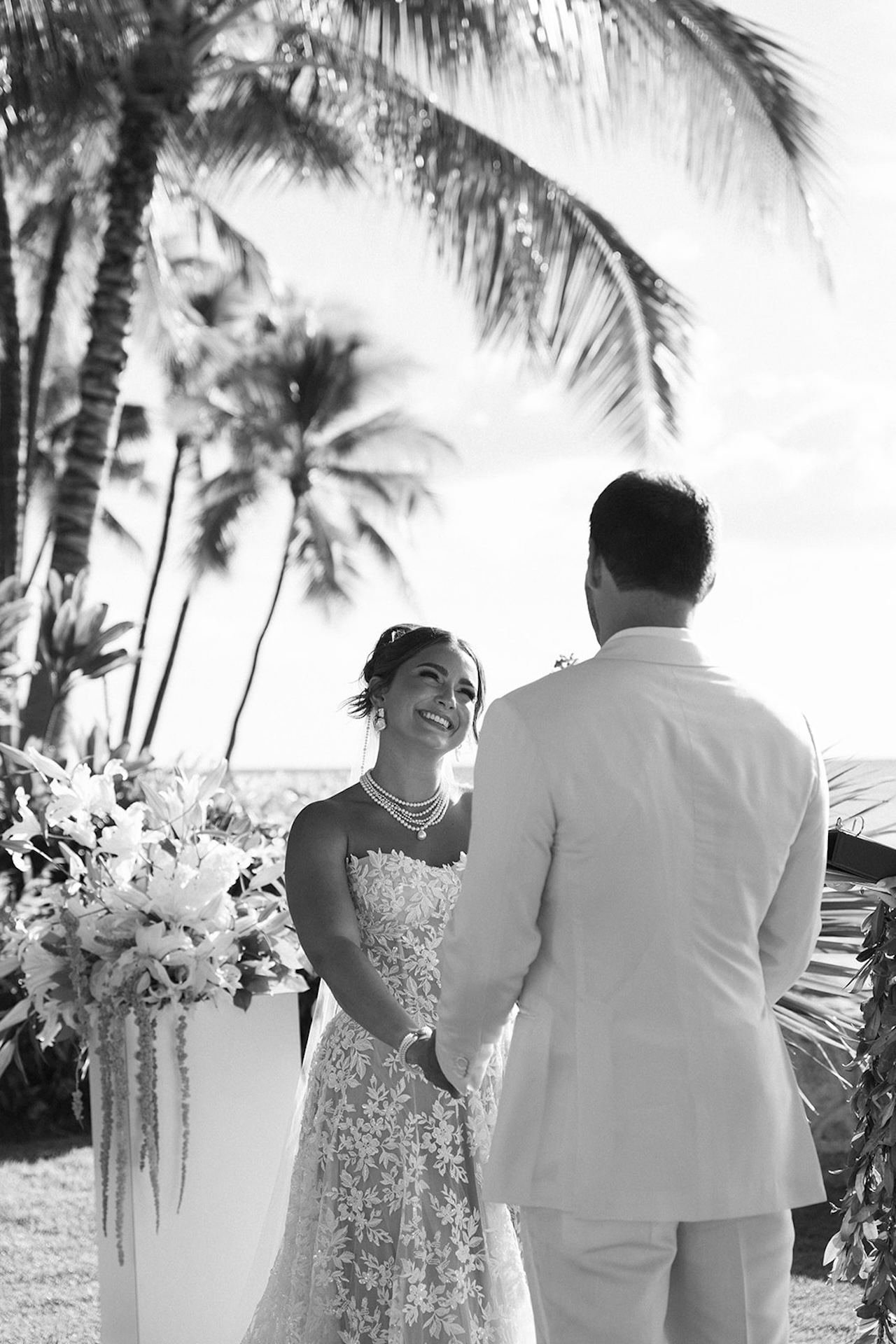 The bride and groom smile at each other during their Lanikuhonua wedding ceremony under the palm trees.