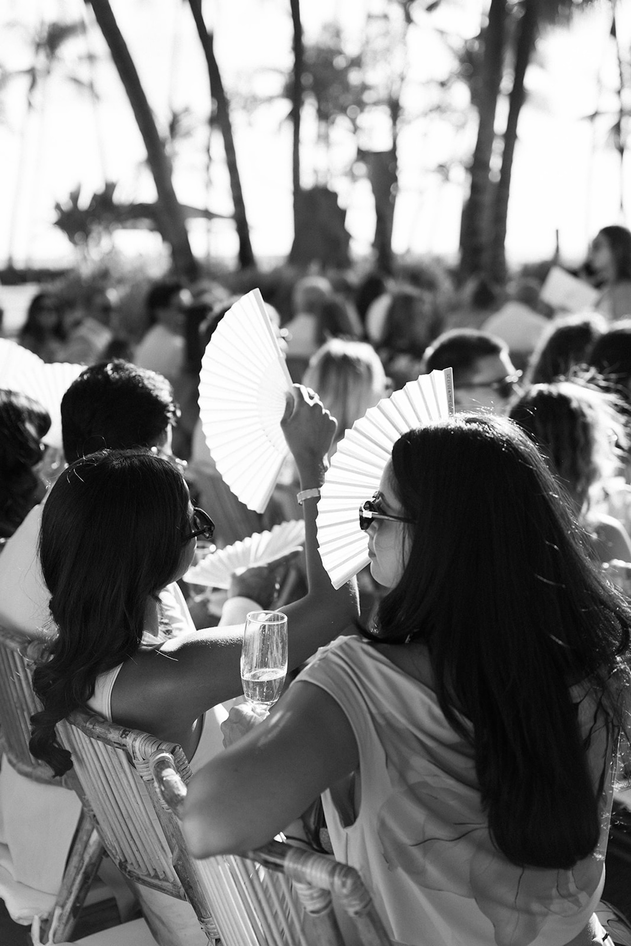 Black-and-white photo of guests fanning themselves while seated at the ceremony.