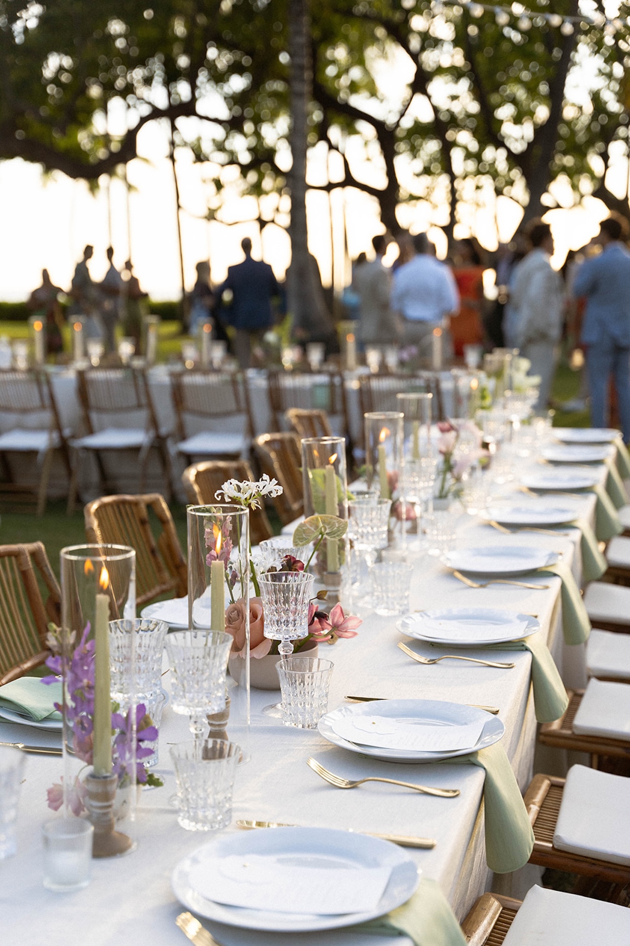 Long reception table set with candles, glassware, and soft pastel florals at sunset.