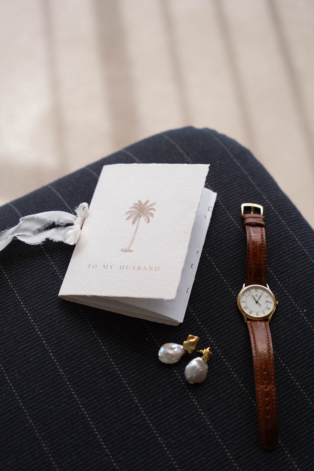 A flatlay image of a "To My Husband" vow book, a watch, and earings for the bride.